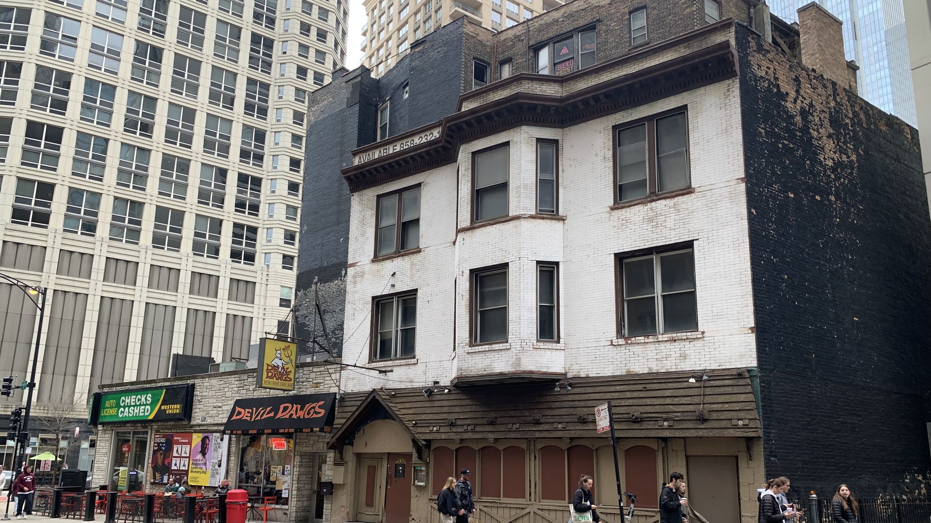 Photo of a house on a street with pedestrians walking by. 