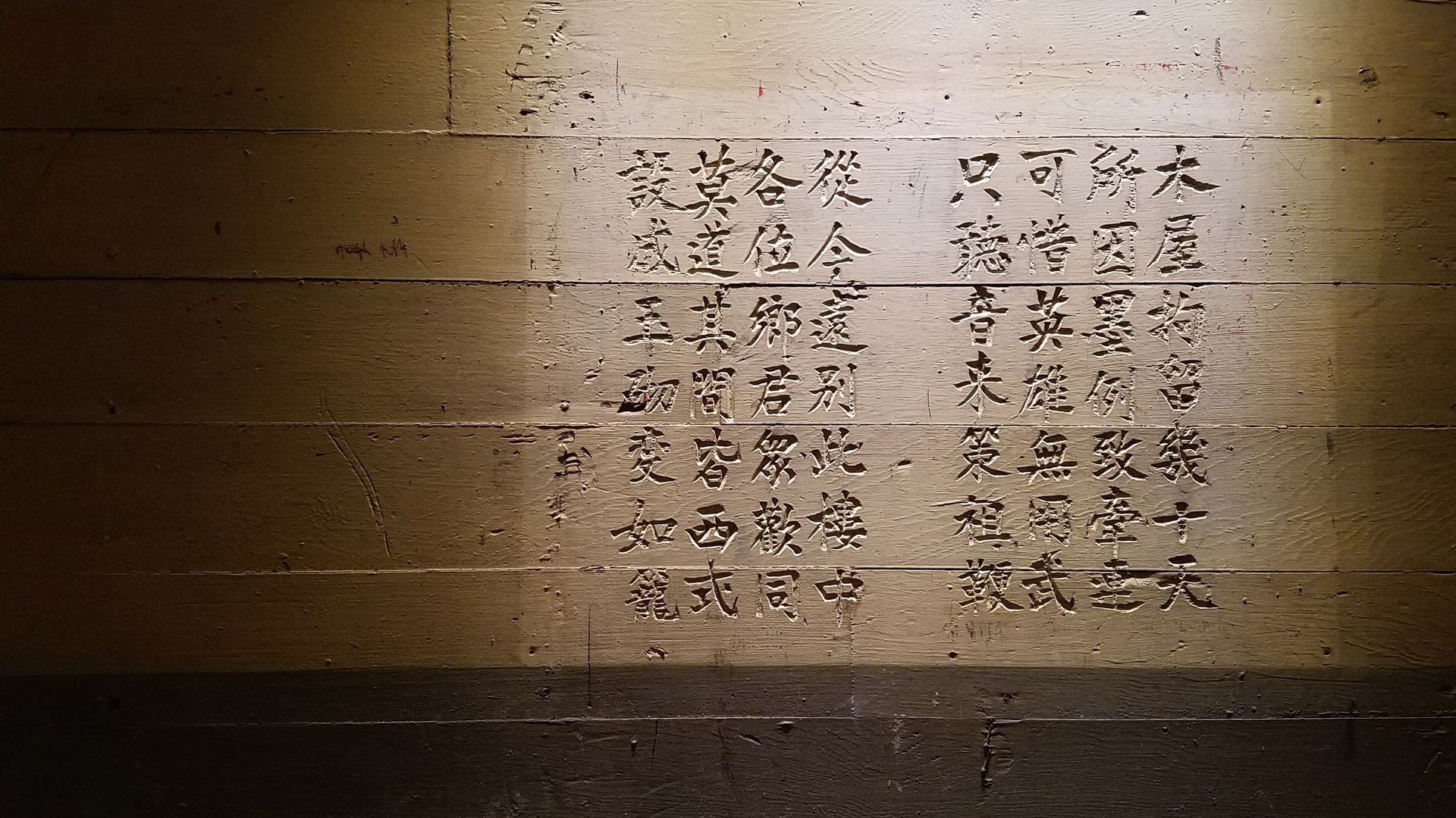 Photo of Chinese characters carved into an old wooden wall with faded brown panels