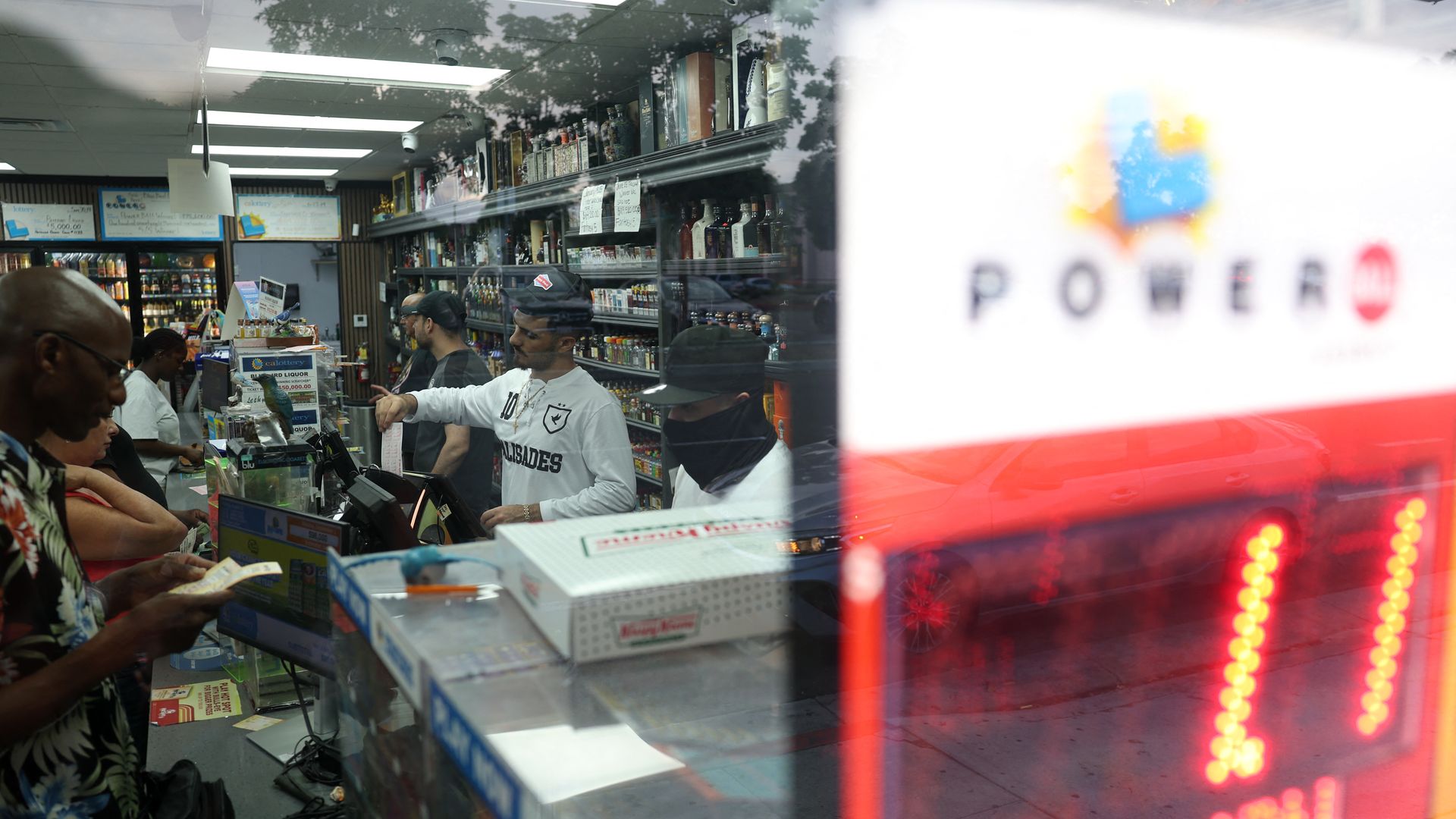 Inside a busy convenience store, customers buy lottery tickets while employees assist at the counter. A bright red digital sign for "PowerBall" lottery shows shows $1.1 billion jackpot.