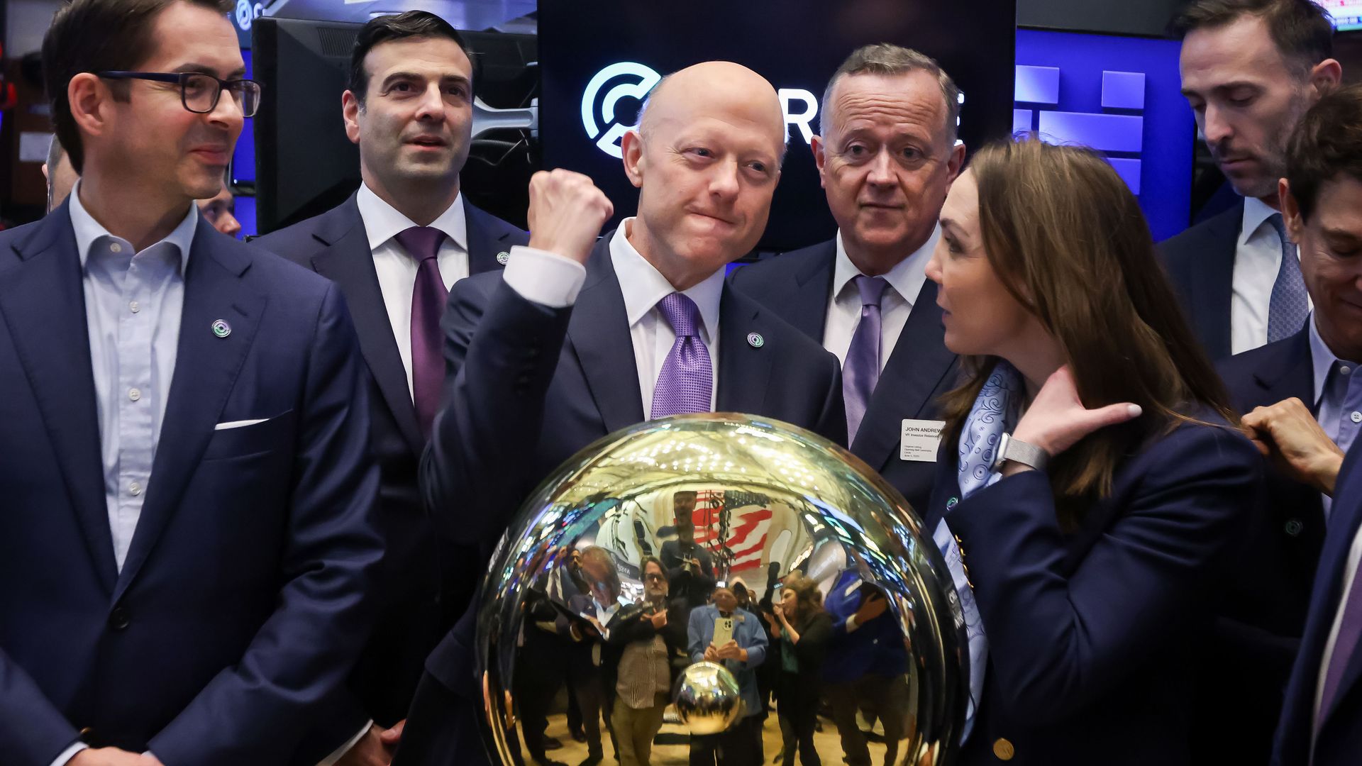Group of people in business attire gathered around a shiny golden sphere at the New York Stock Exchange, celebrating Circle Internet Group's stock listing shown on monitors above.