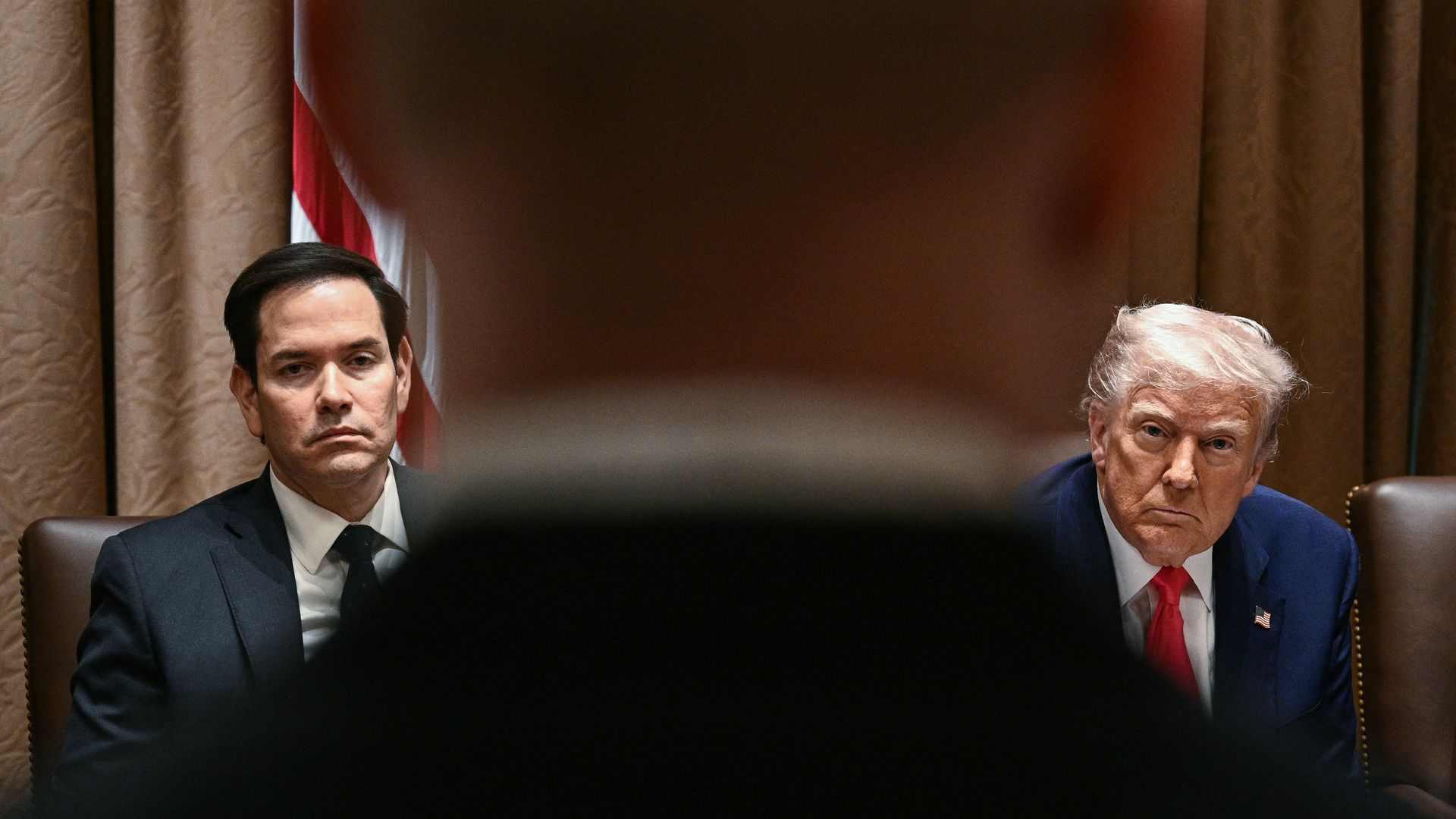 Secretary of State Marco Rubio (left) and President Trump are shown separated by someone in the foreground.