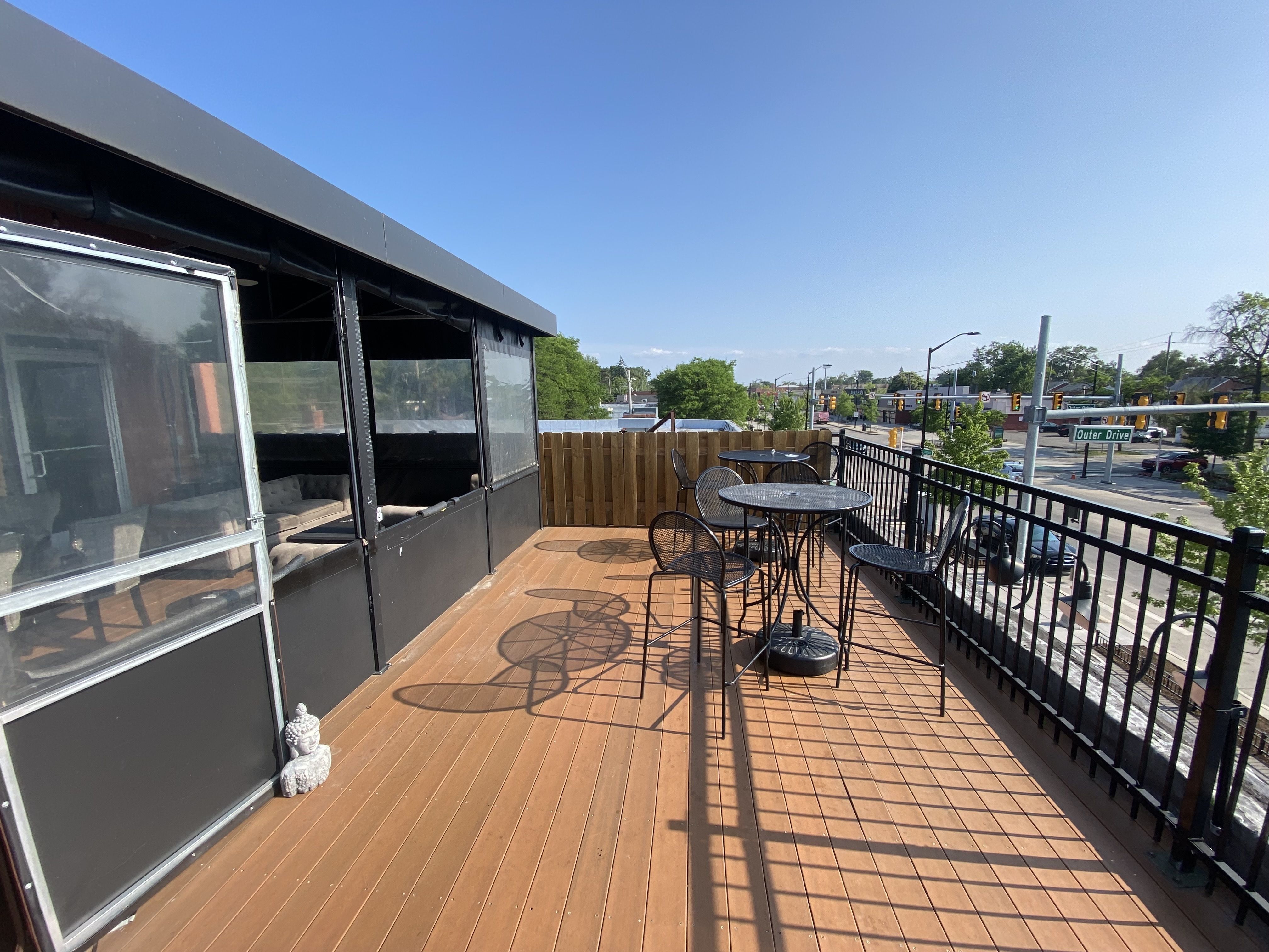 Chairs are on a sunny patio overlooking a commercial corridor.
