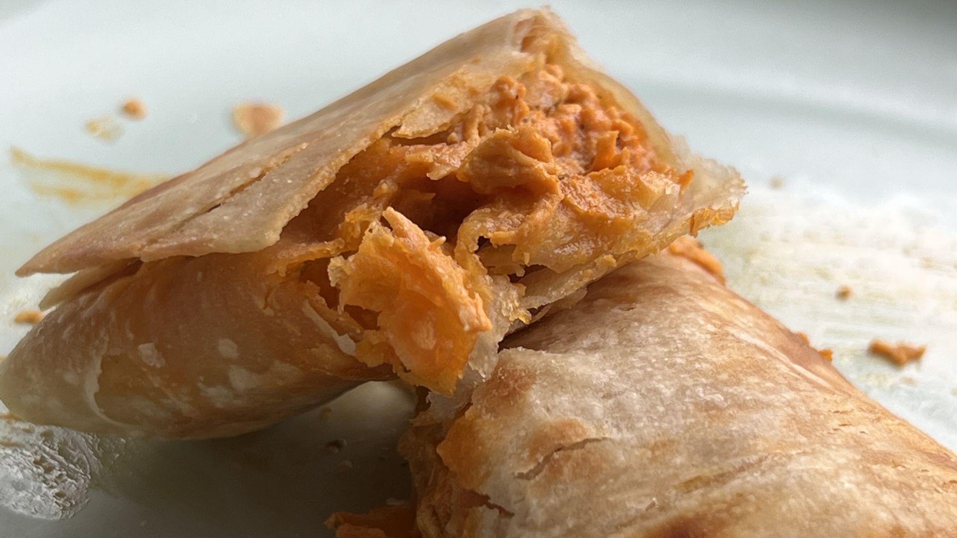Close-up of a flaky croissant-like pastry with orange filling, bitten into, revealing layered, crumbly interior on a pale plate.