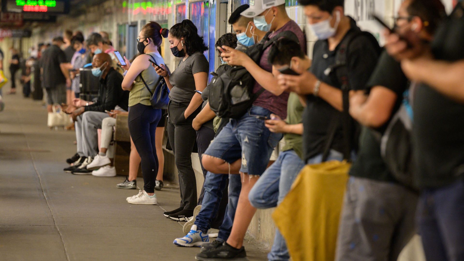 Commuters looks at their mobile phones as they wait for a subway train in New York on June 10, 2021.