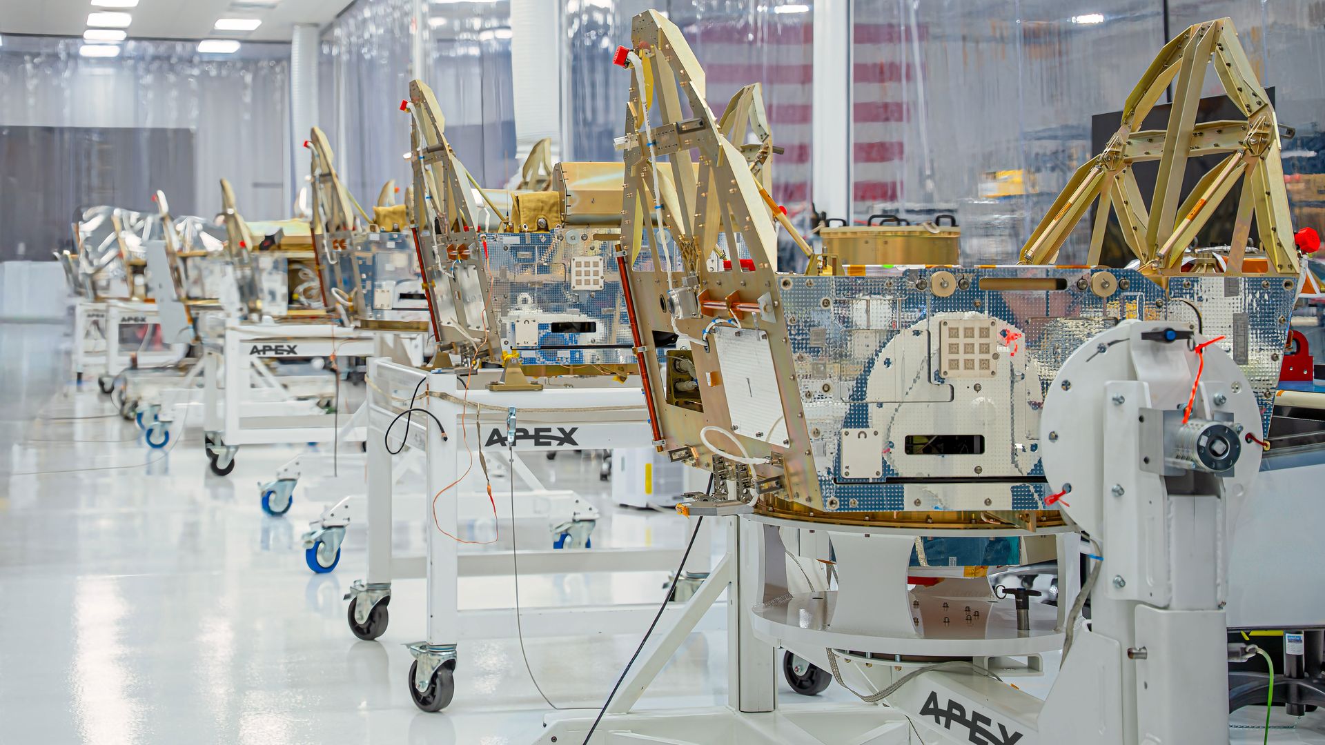 Bright aerospace lab with multiple beige metal frame structures on wheeled carts, exposed circuitry and wiring.