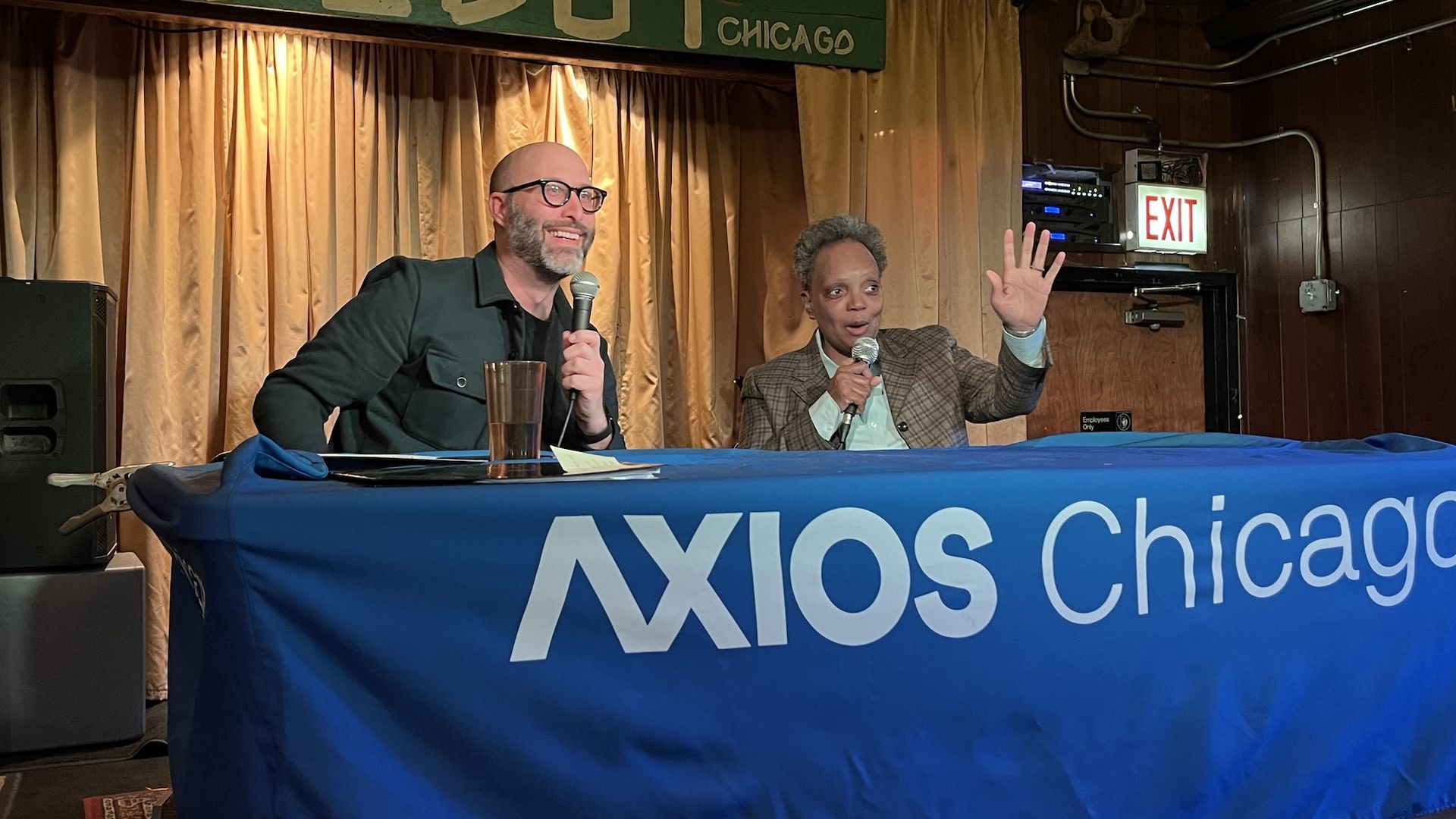 A man holding a microphone next to a woman holding a microphone sitting at a table with a blue tablecloth that reads: Axios Chicago.