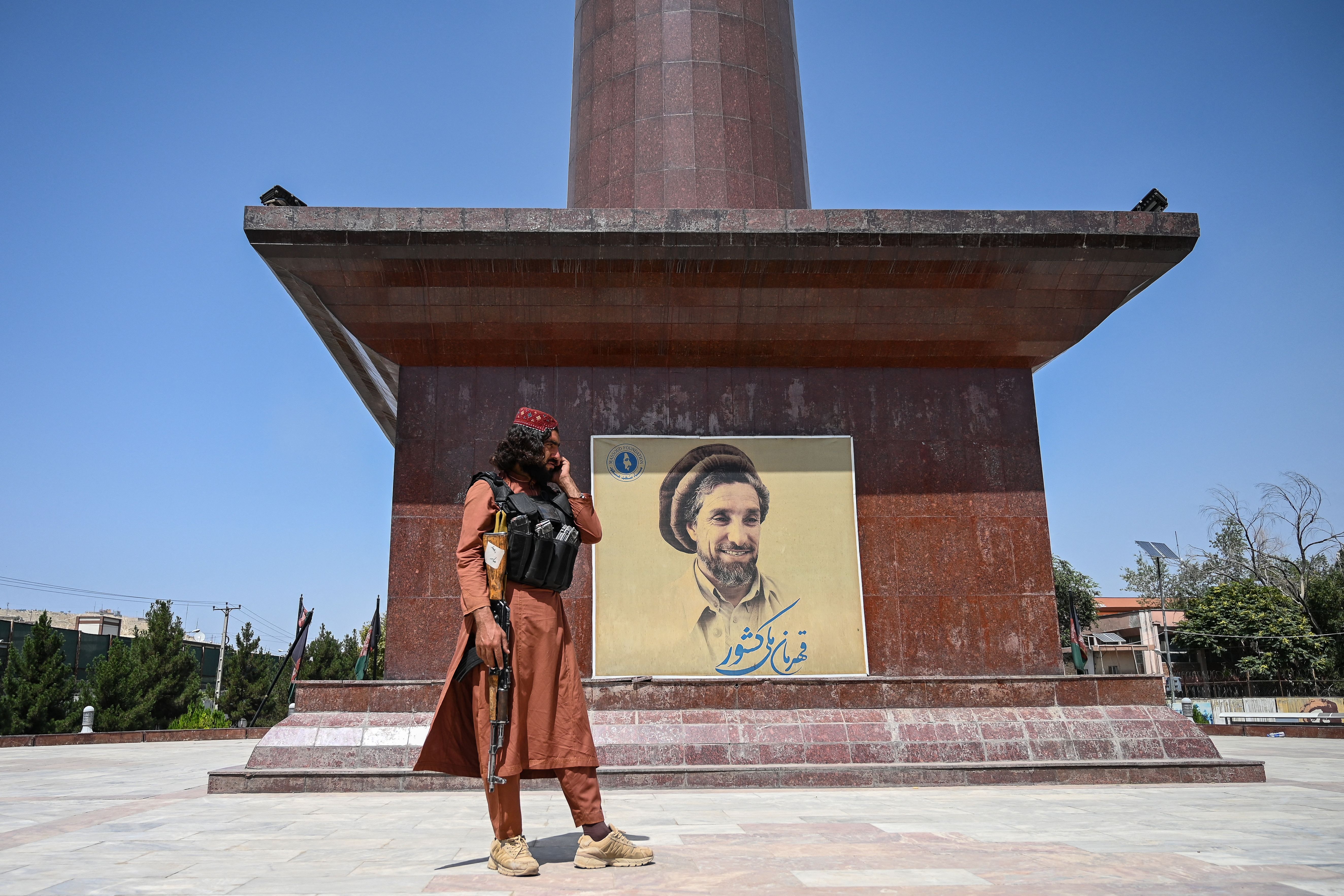 A Taliban fighter stand next to poster bearing the image late Afghan commander Ahmad Shah Massoud at the Massoud Square in Kabul on August 16