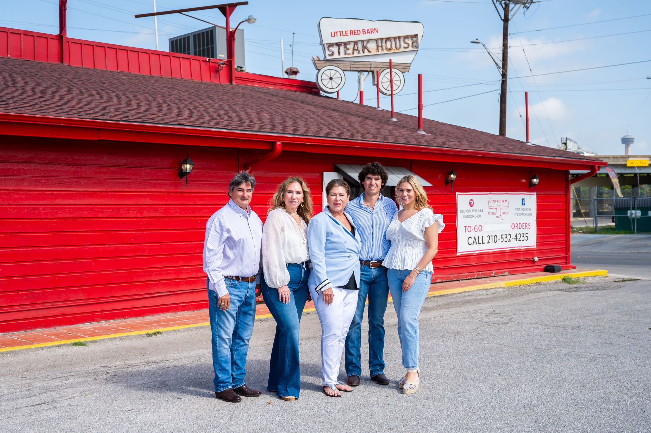A group of five people stand outside a red restaurant building. 