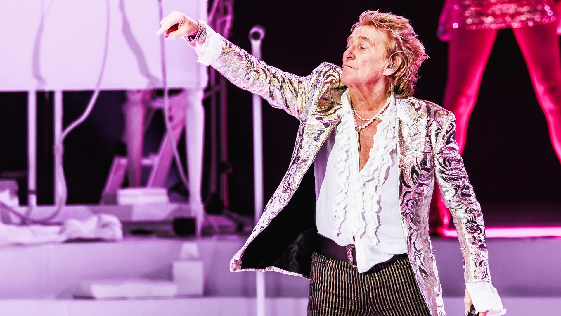 Rod Stewart on stage, lifting his hand to the audience