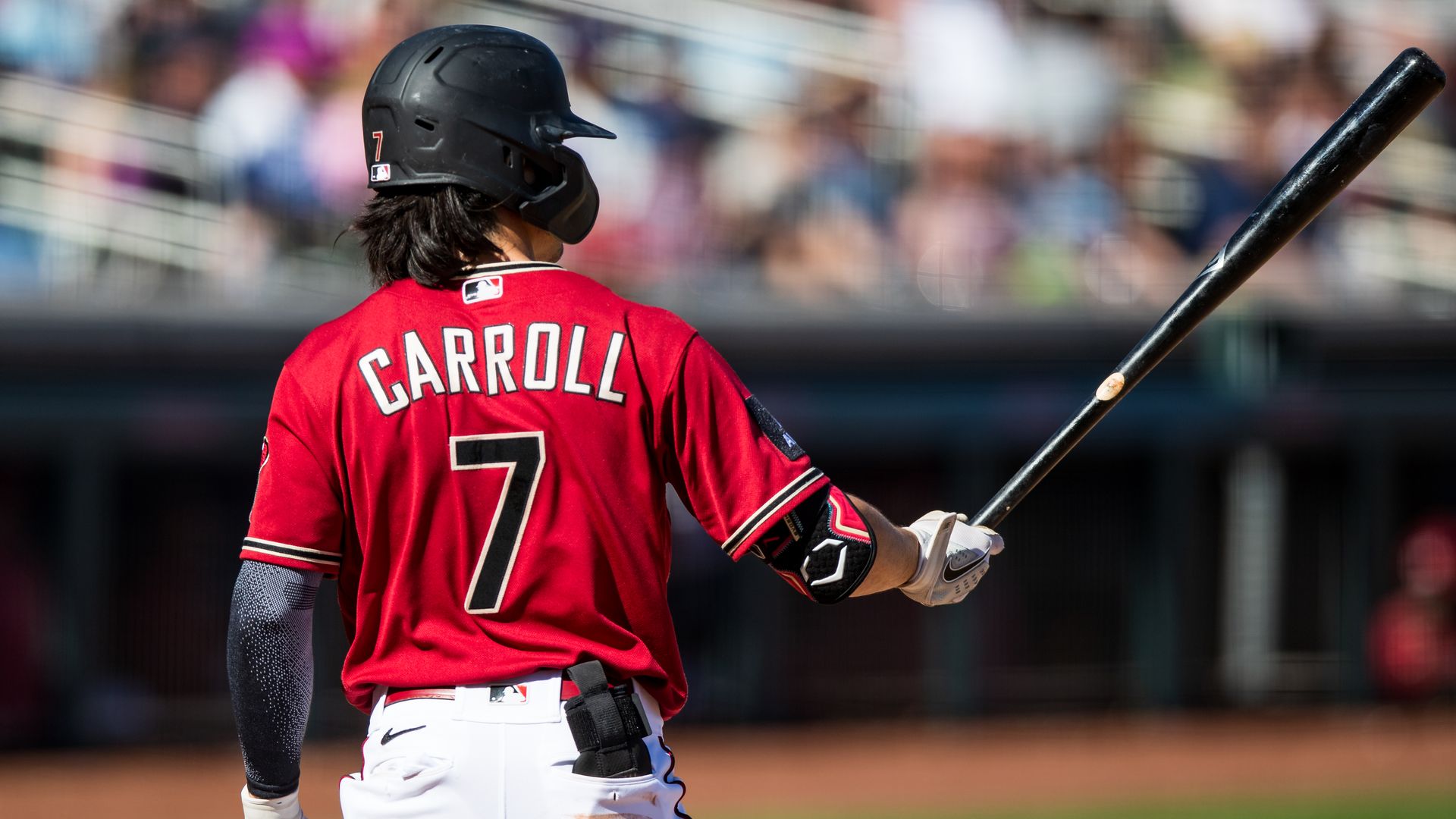 A picture from behind of a baseball player in a red uniform holding up a bat to his side.