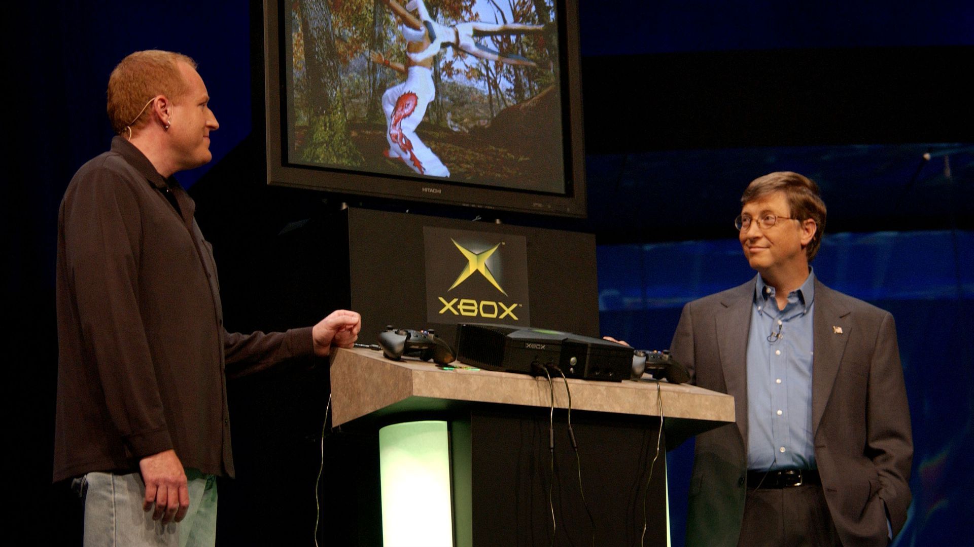 Photo of Seamus Blackley and Bill Gates standing on stage with an Xbox console in between them