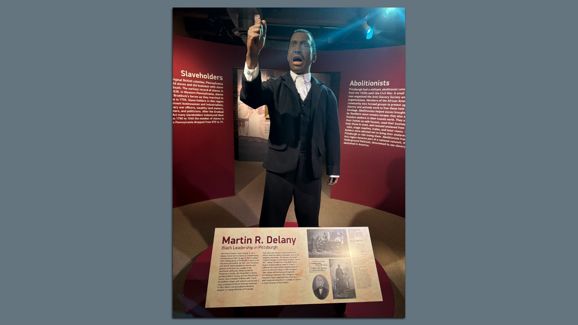 Exhibit showing a statue of Martin R. Delany in black suit with raised hand, surrounded by panels about slaveholders and abolitionists, detailing his leadership in Pittsburgh.