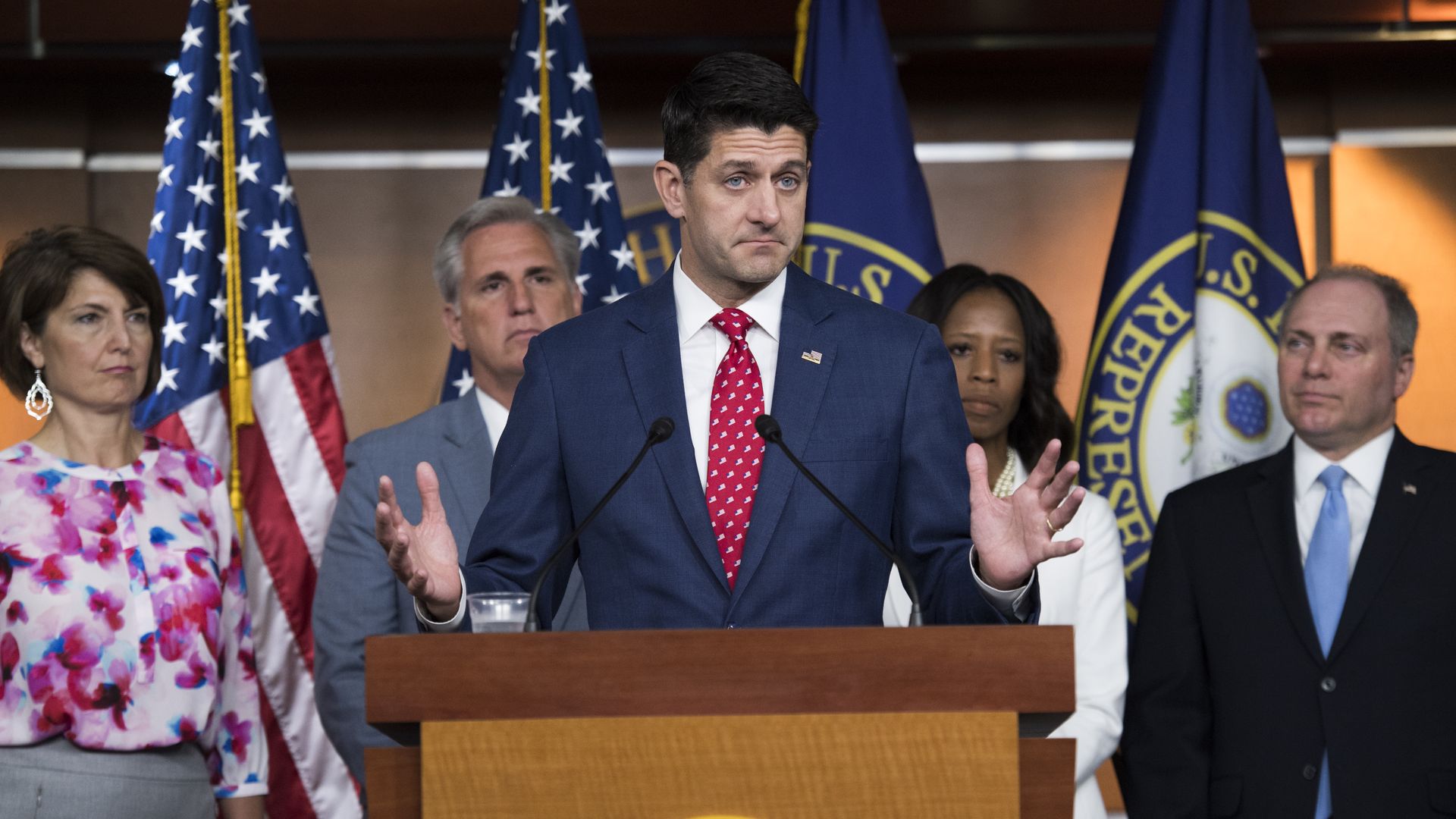 Paul Ryan speaking at a podium with his hands in the air and his bottom lip jutted out