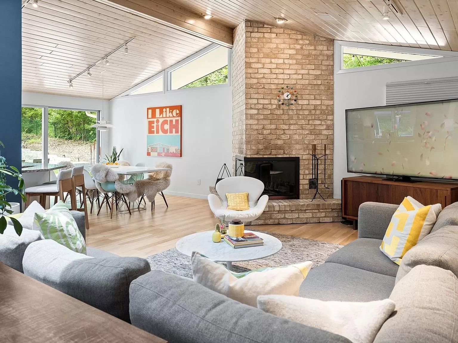 A living room with a fireplace, gray couch and dining room table.