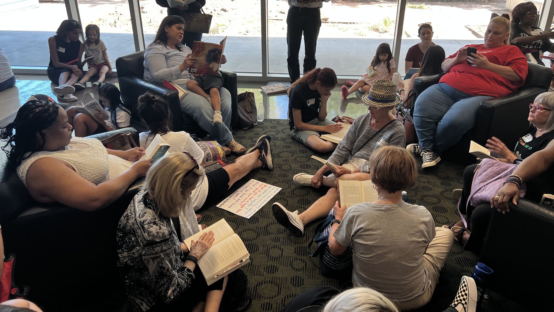 A group of people read books in chairs, on the floor and while standing during a read-in protest at the Houston ISD headquarters