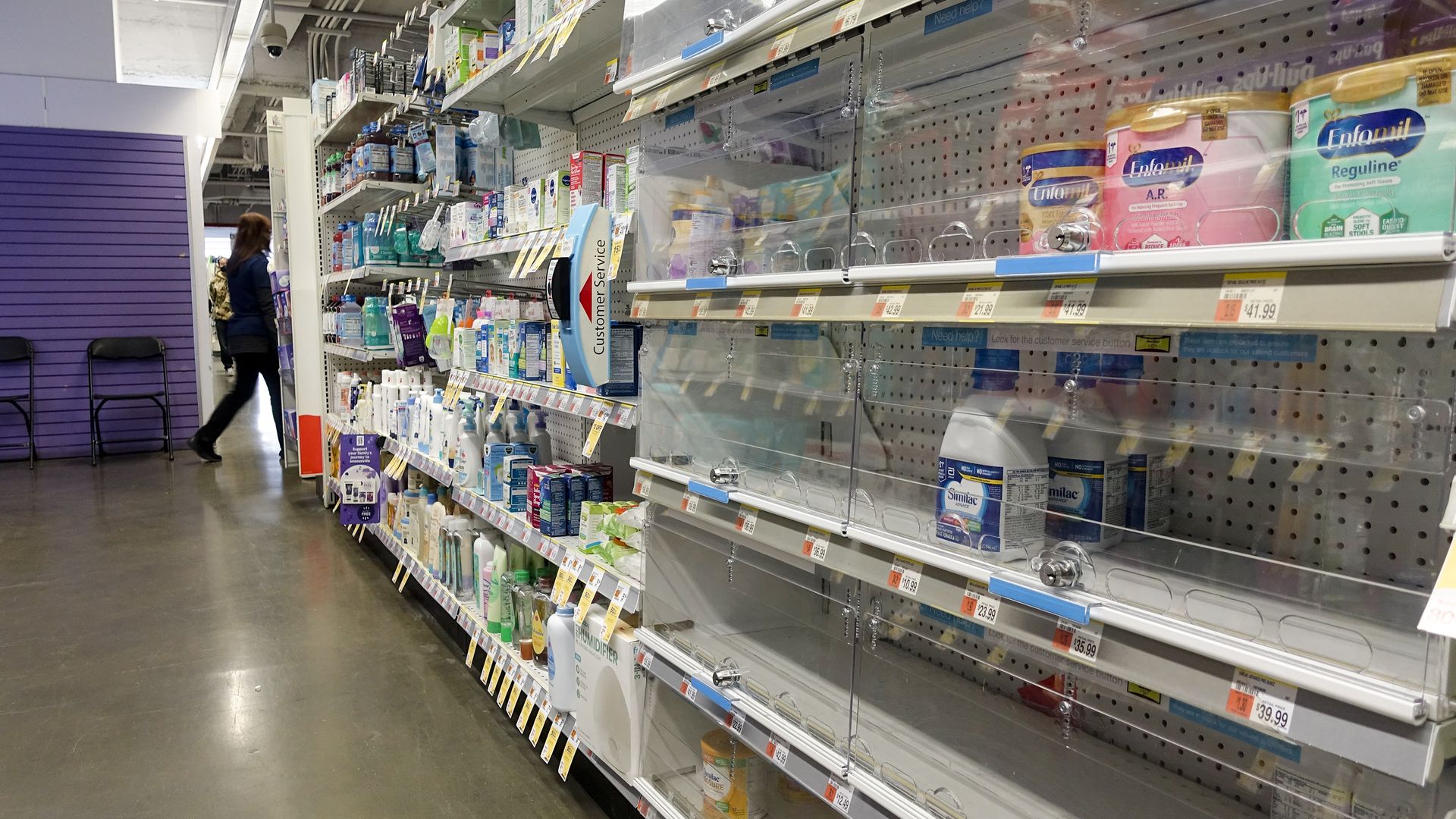 Largely empty shelves of baby formula behind a glass case