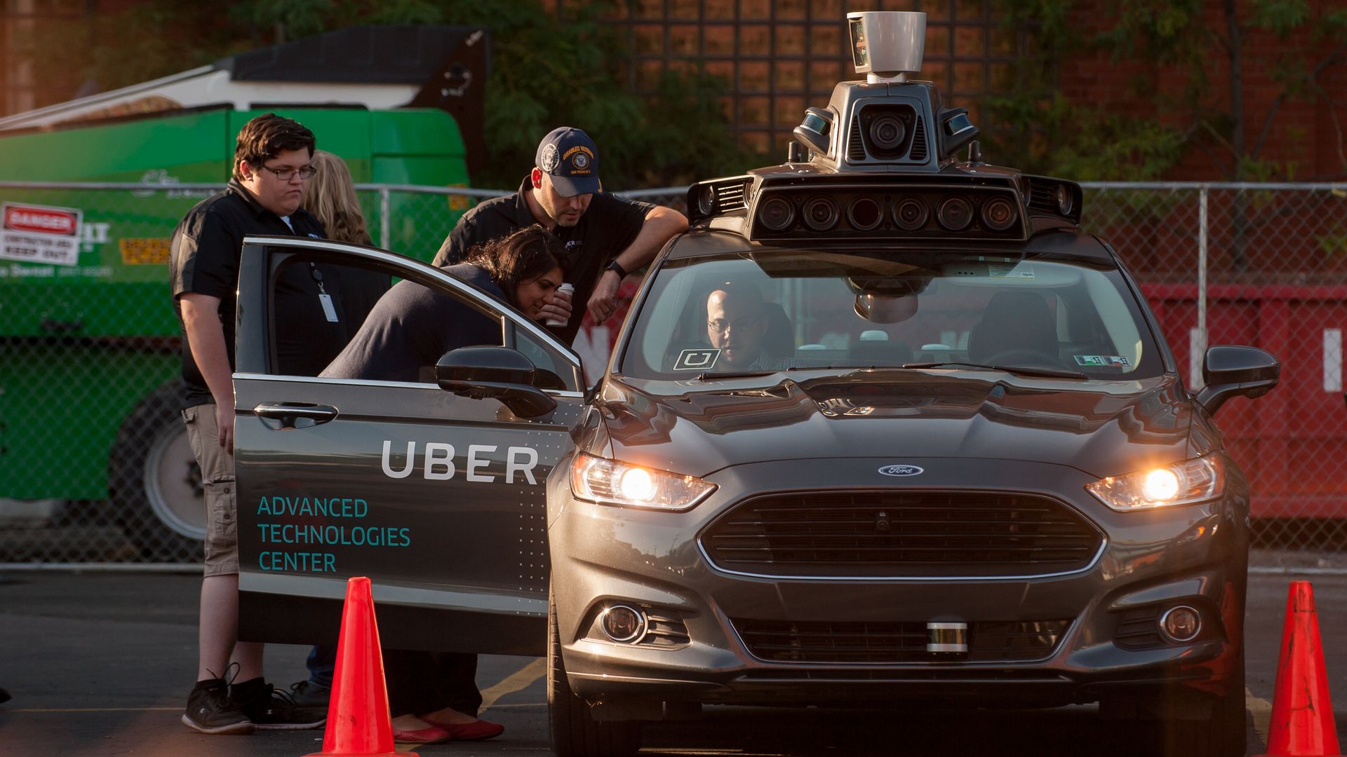 people crowd around a self-driving Uber vehicle in a parking lot
