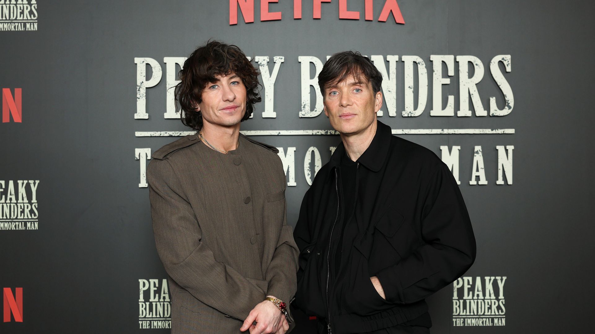 Two men pose together at a red-carpet event in front of a gray backdrop featuring the Netflix logo and the title “Peaky Blinders: The Immortal Man.”