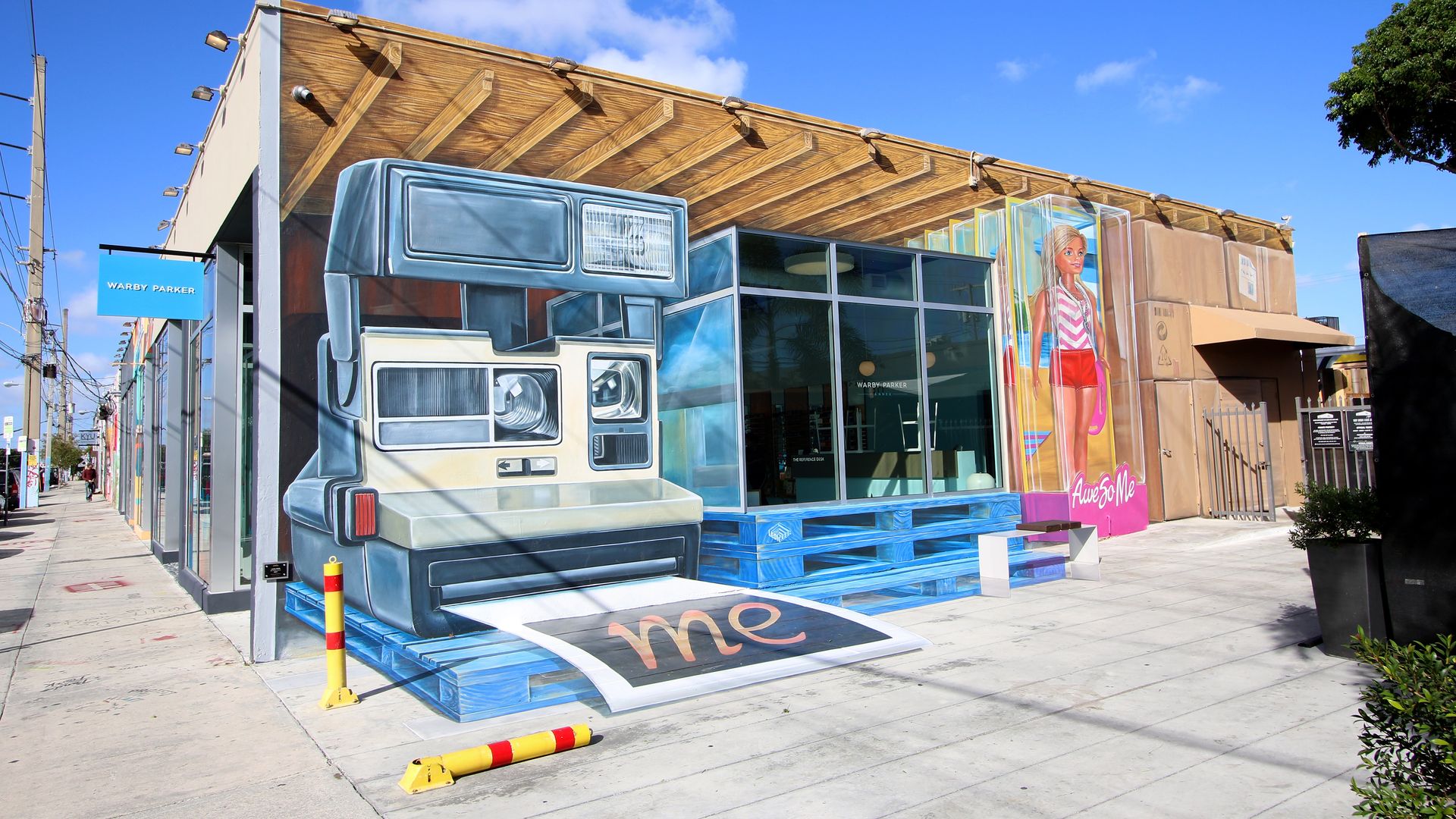 Building mural of a giant vintage Polaroid camera printing a photo labeled \