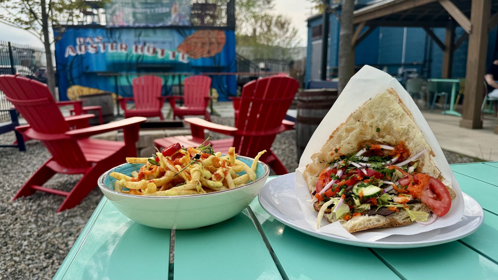 a brightly colored sandwich and fries with a patio shown behind, including chairs and a shipping container.