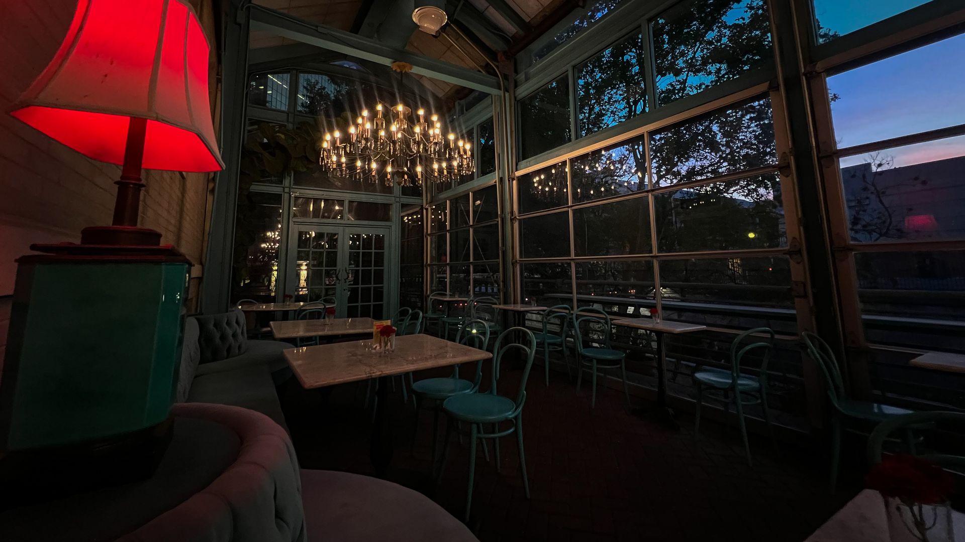 A dining space inside a low-lit greenhouse decorated with elegant lamps and chandeliers.