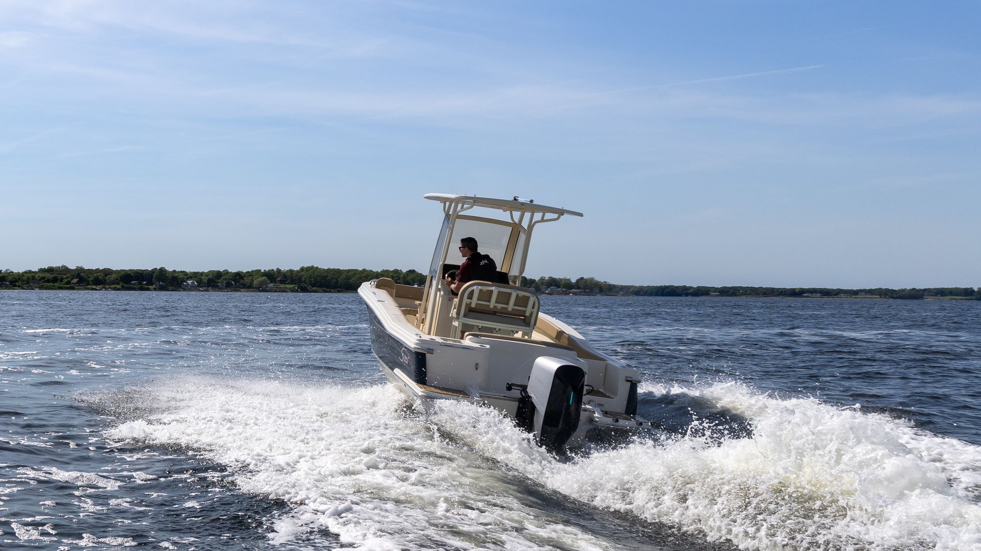 A white, 22-foot boat outfitted with a gray-and-black, electric outboard motor from Flux Marine, motors across smooth waters beneath sunny blue skies in Bristol Bay, Rhode Island.