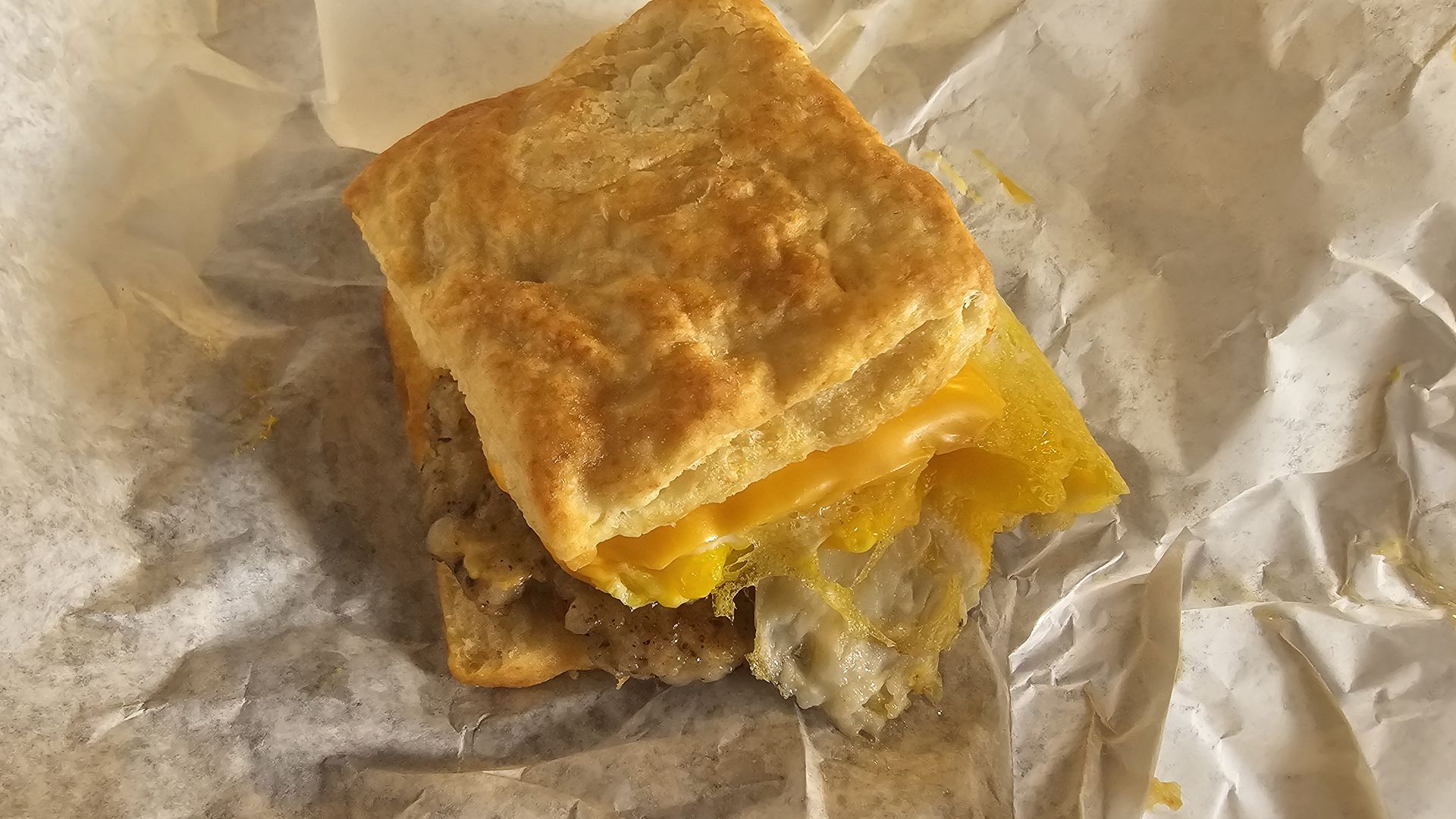 A golden, flaky pastry sandwich with melted yellow cheddar, resting on crinkled aluminum foil.
