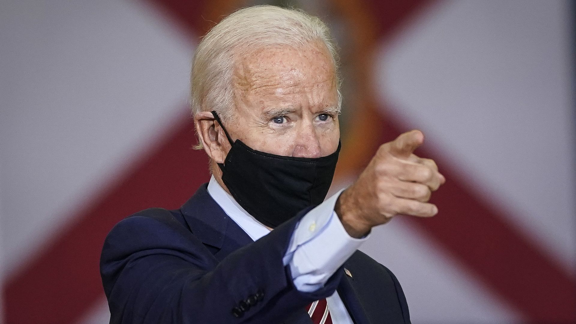 Joe Biden wearing a black face mask and pointing his left index finger