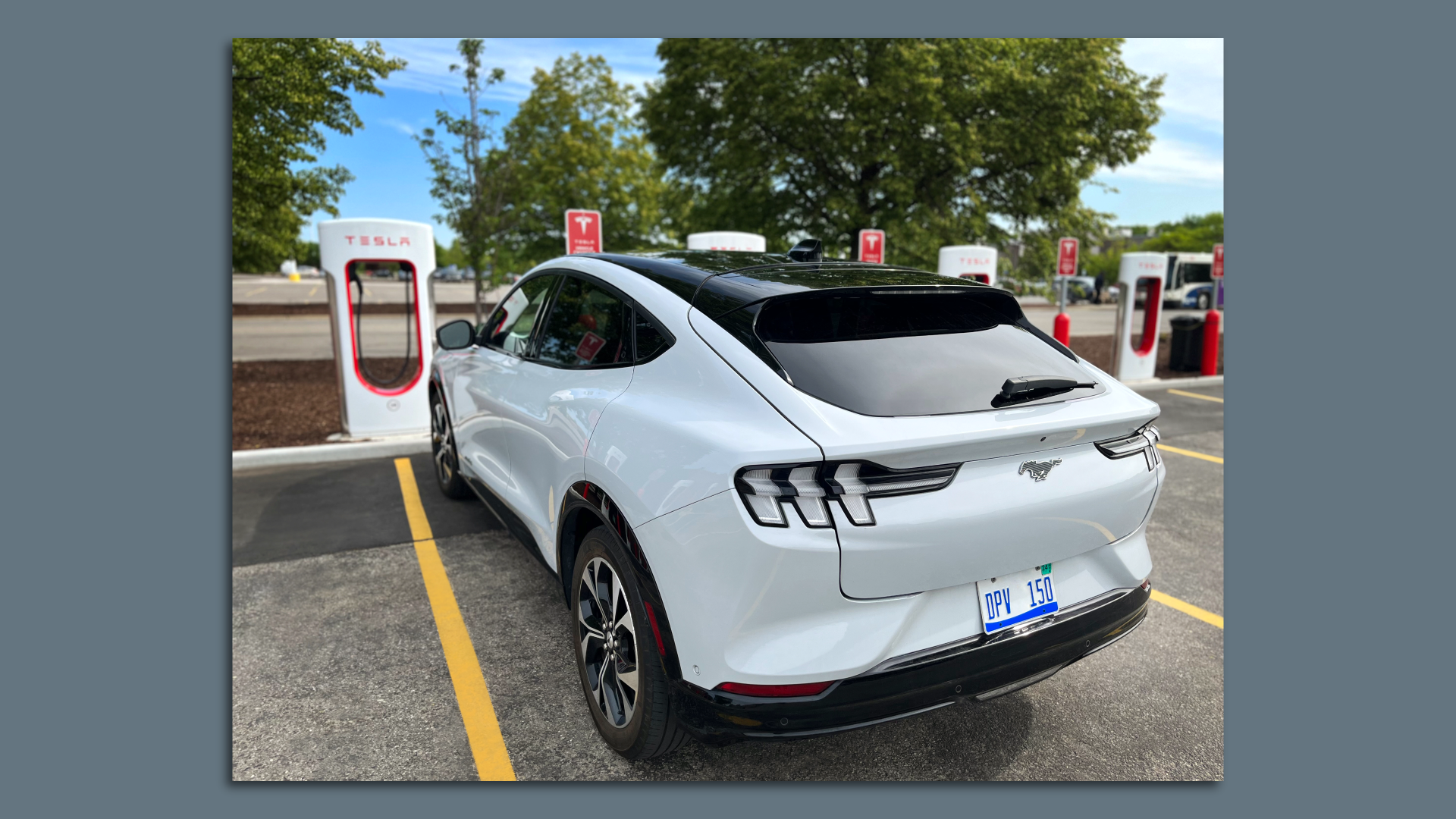 Image of a white Ford Mustang Mach-e plugged into a Tesla Supercharger