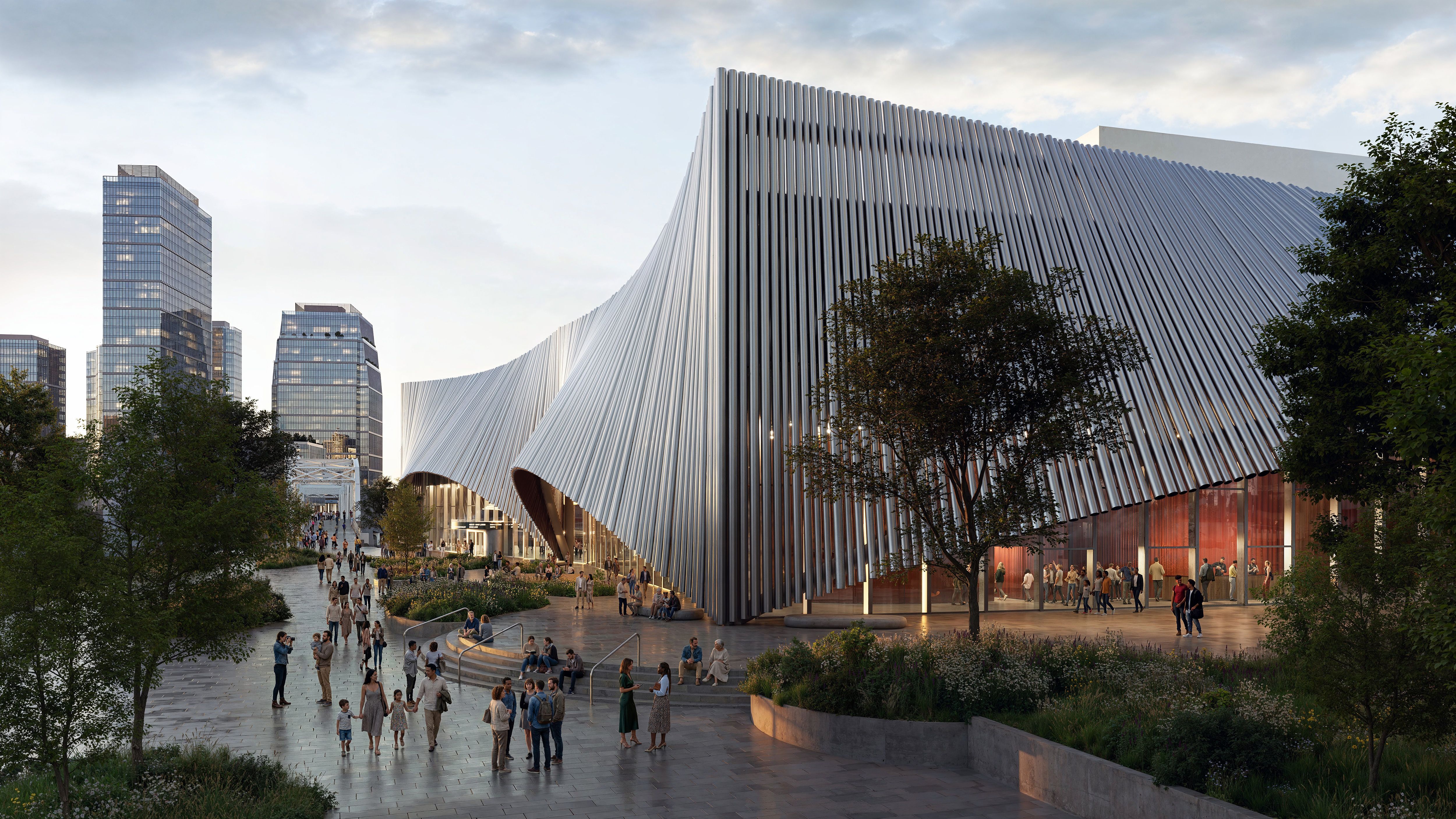 Public plaza featuring a dramatic, wavy ribbed metal building; glass towers rise in the background as people walk among trees and planters at dusk.