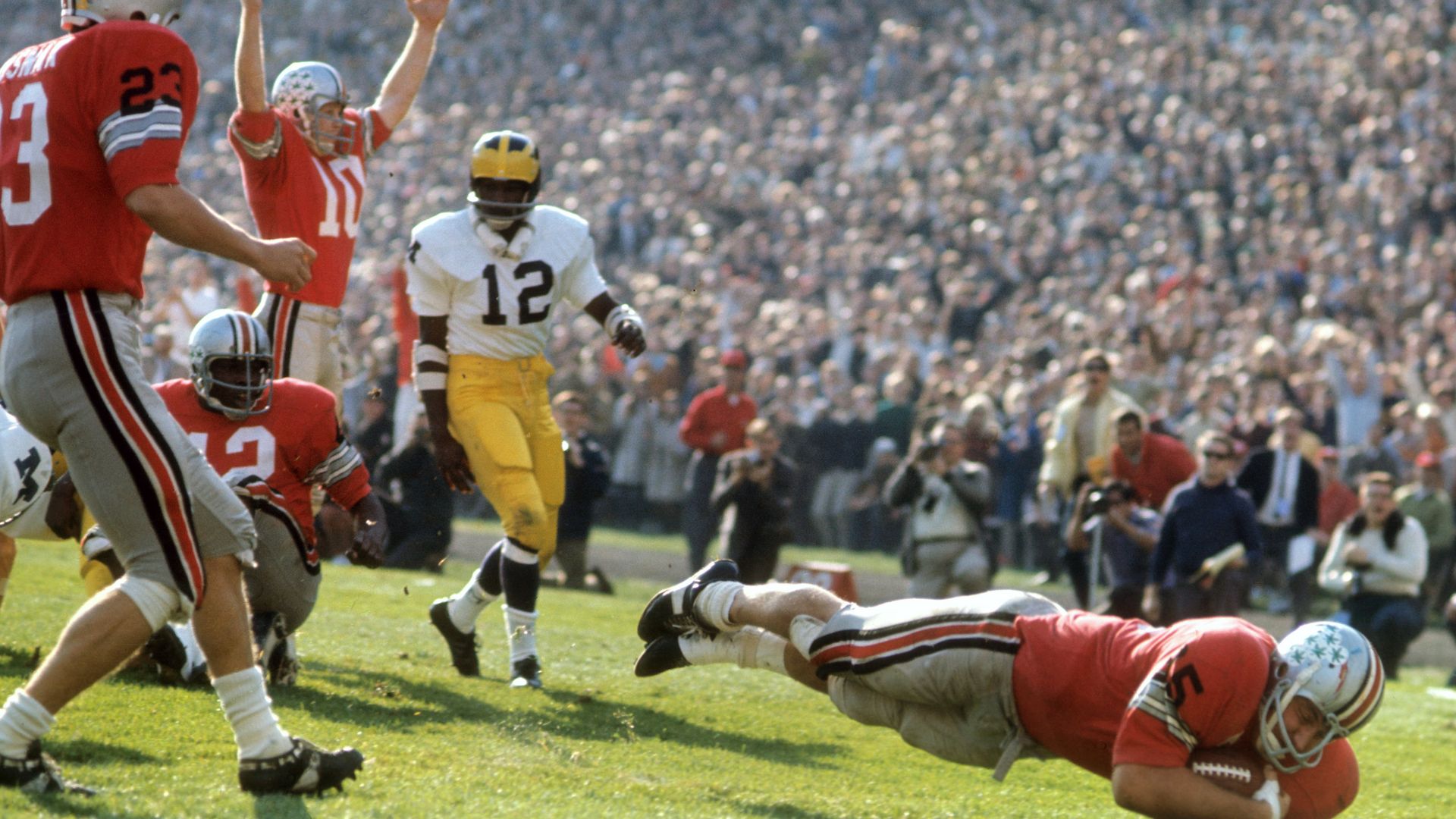 A football player dives for the ball as others look on.