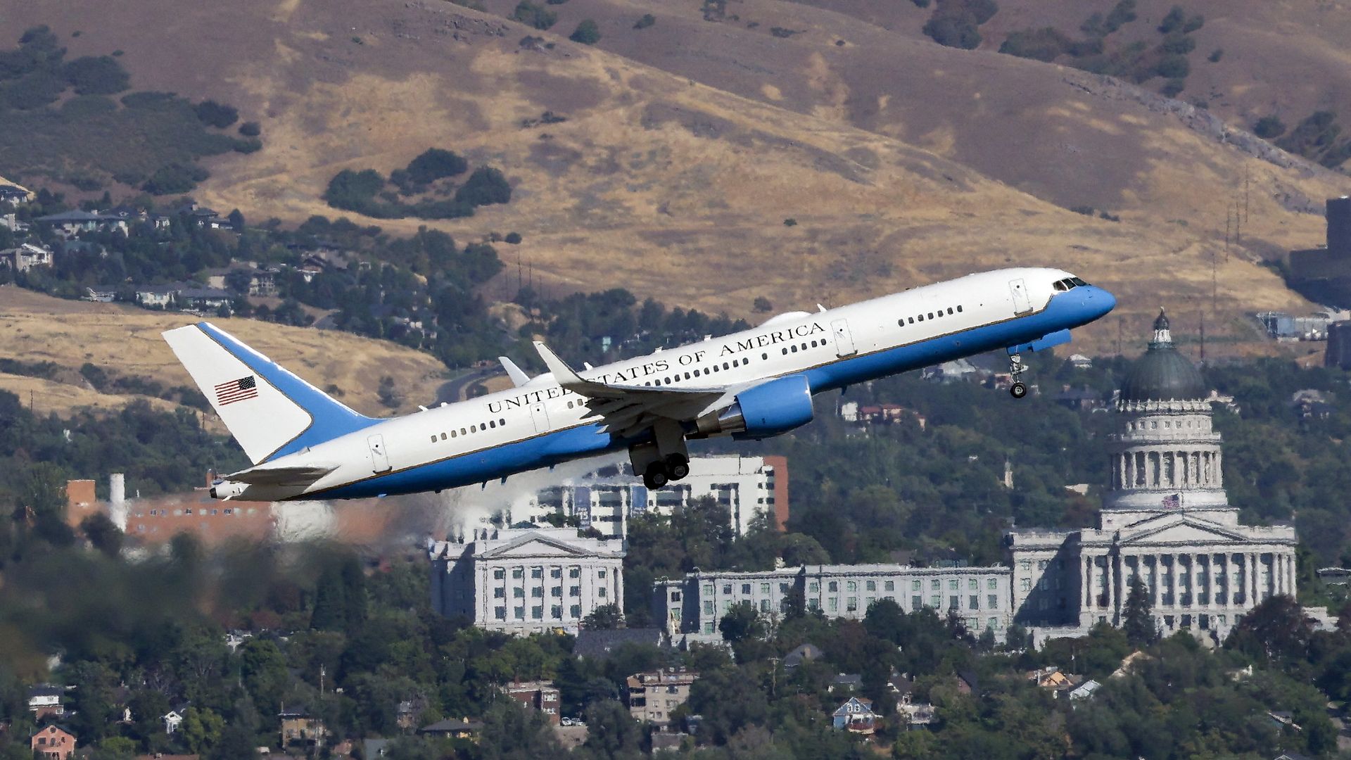 A white and blue airliner with "United States of America" painted on the side ascends, with the Utah state Capitol in the background.