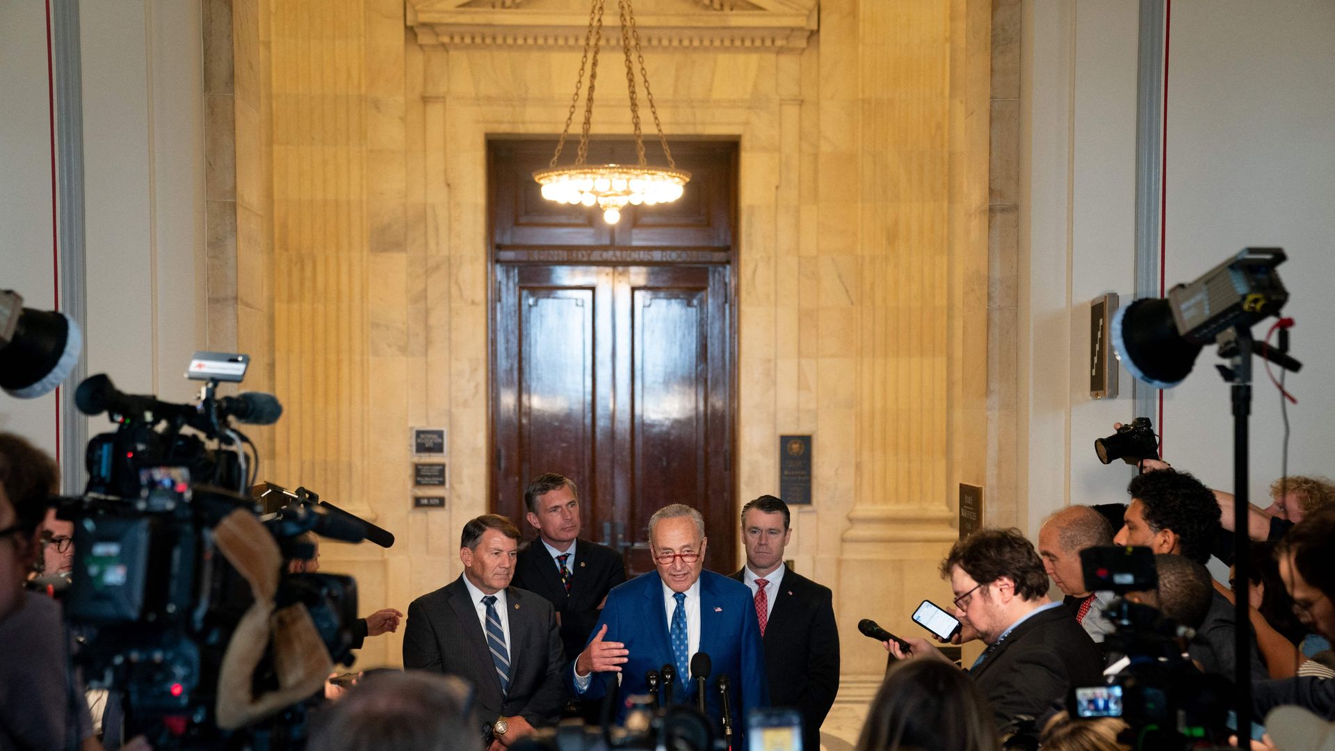 Four people stand in front of a crowd with microphones and cameras