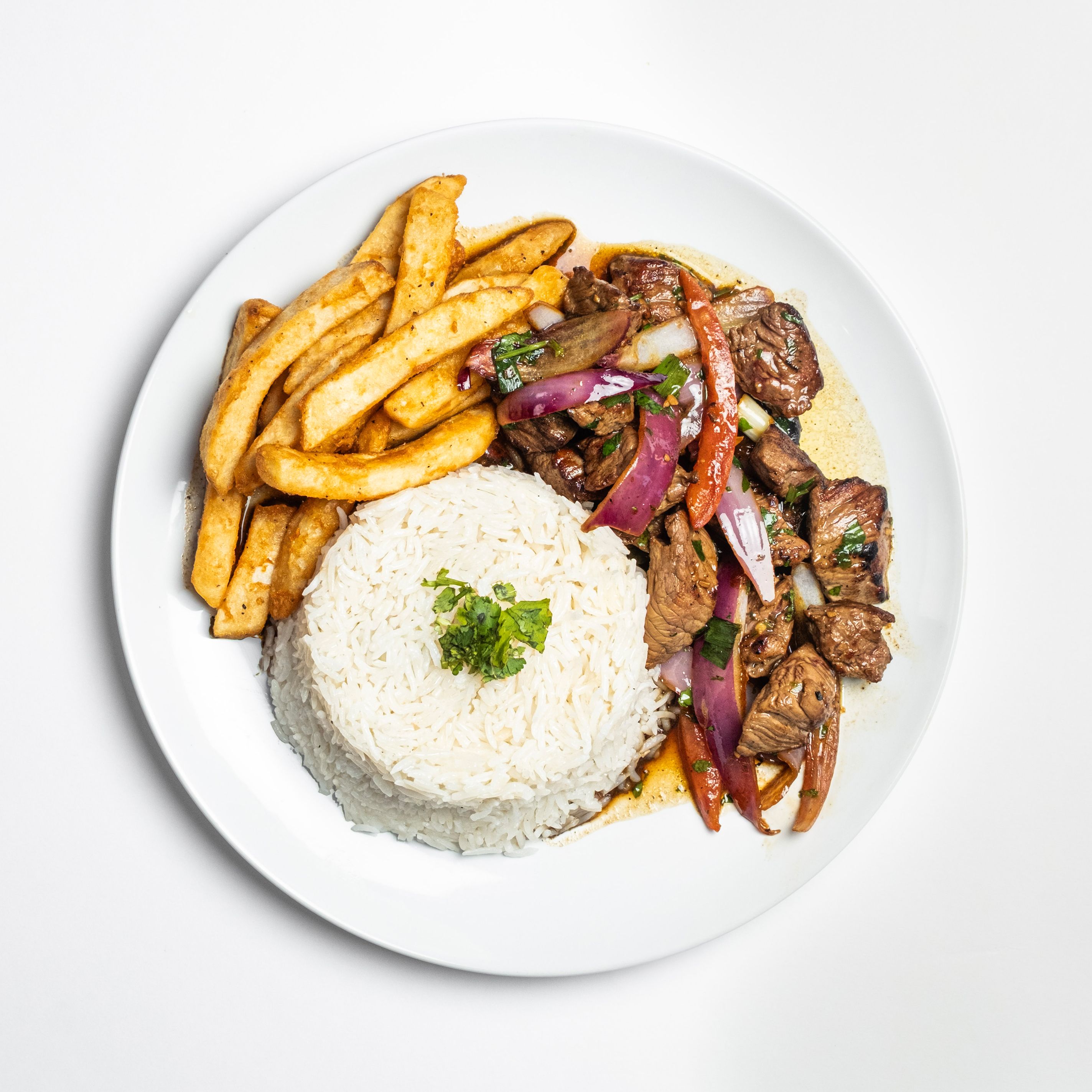 White plate holds a mound of steamed white rice with parsley, a side of golden fries, and sautéed beef with red onions and bell peppers.