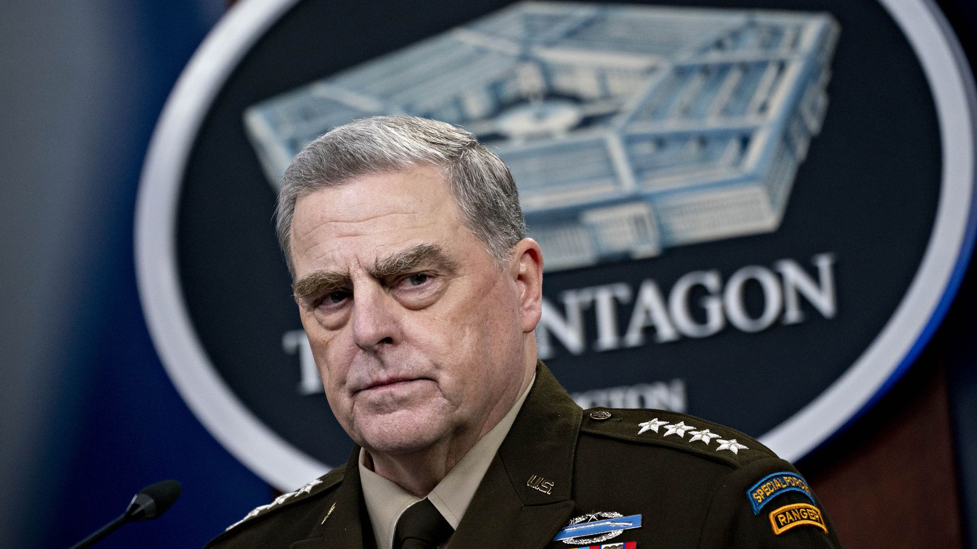 A close-up of Joint Chiefs Chairman Mark Milley, with an intense look on his face, in front of a seal of the Pentagon 