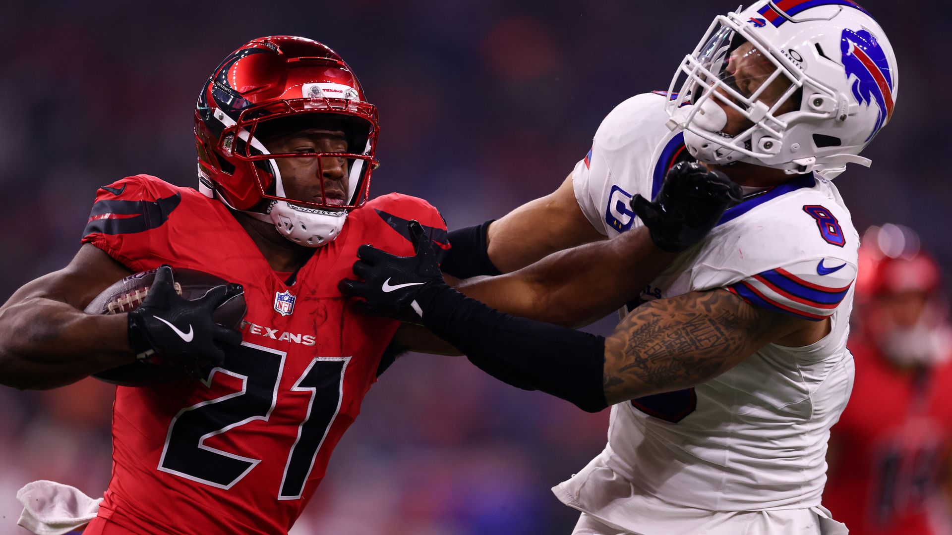 A Texans player in red carrying the football stiff arms a Buffalo Bills player in white