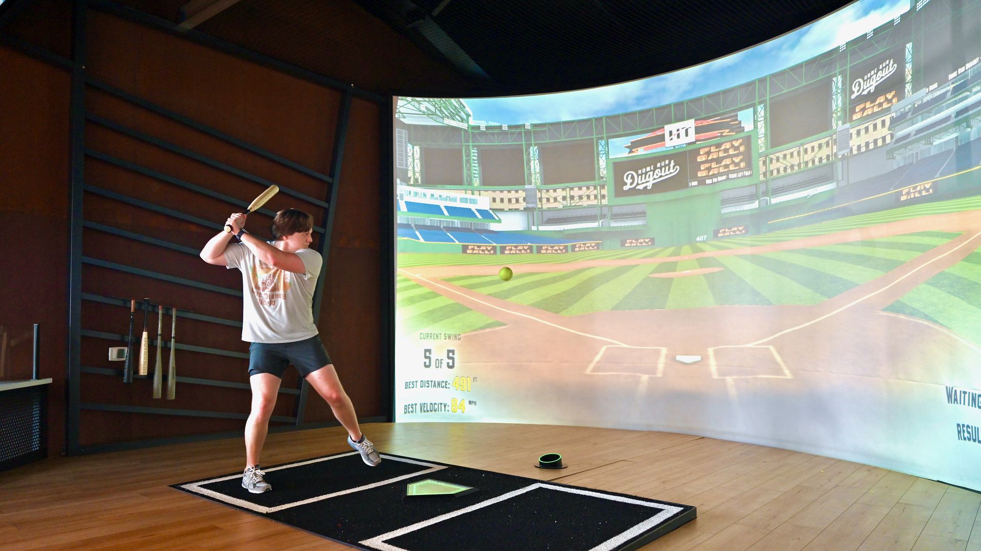 A man prepares to swing a baseball bat in front of a virtual display of a baseball diamond in a ballpark. 