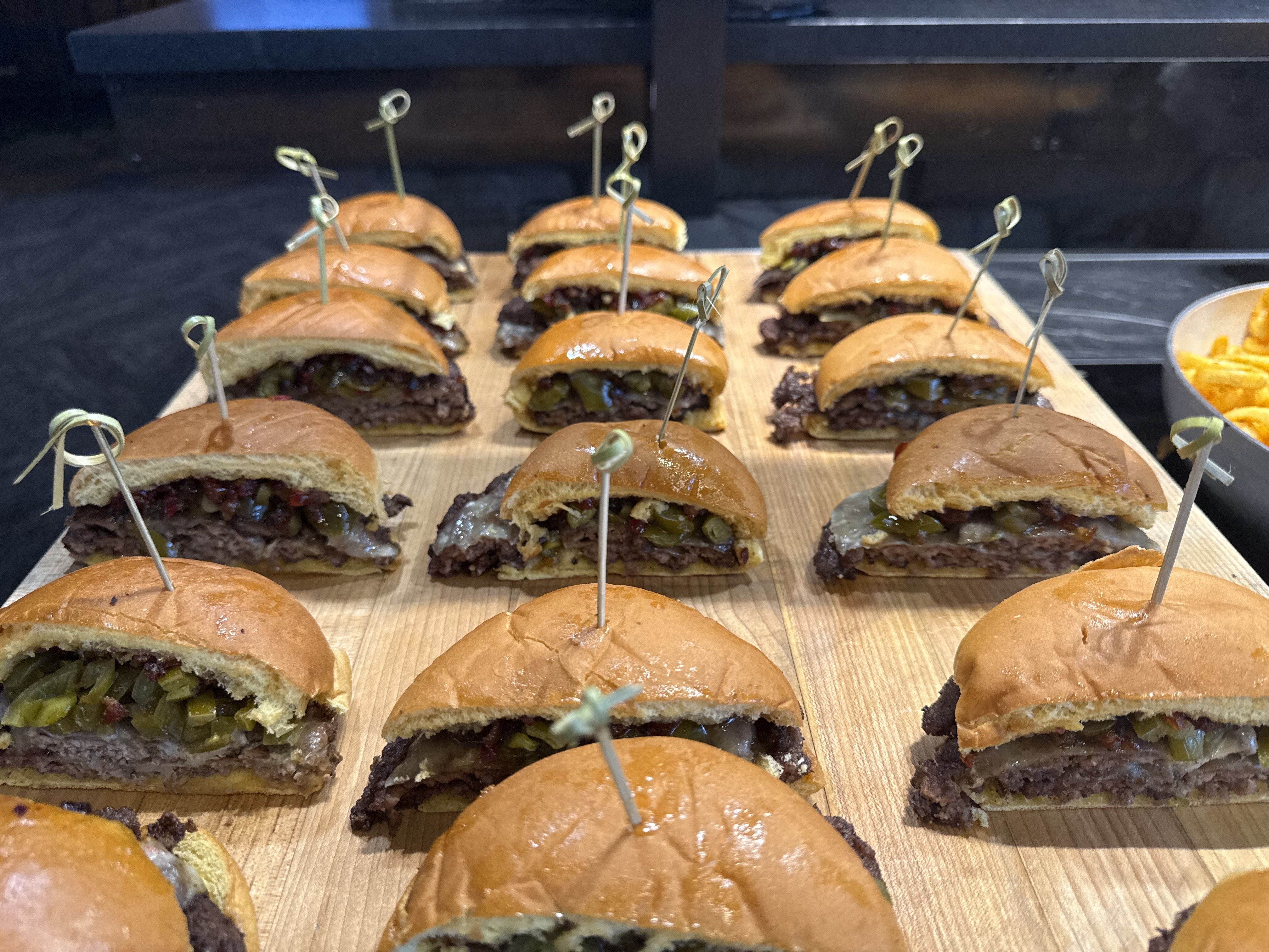 Several small burgers are lined up, with thick patties and jalapeños. 