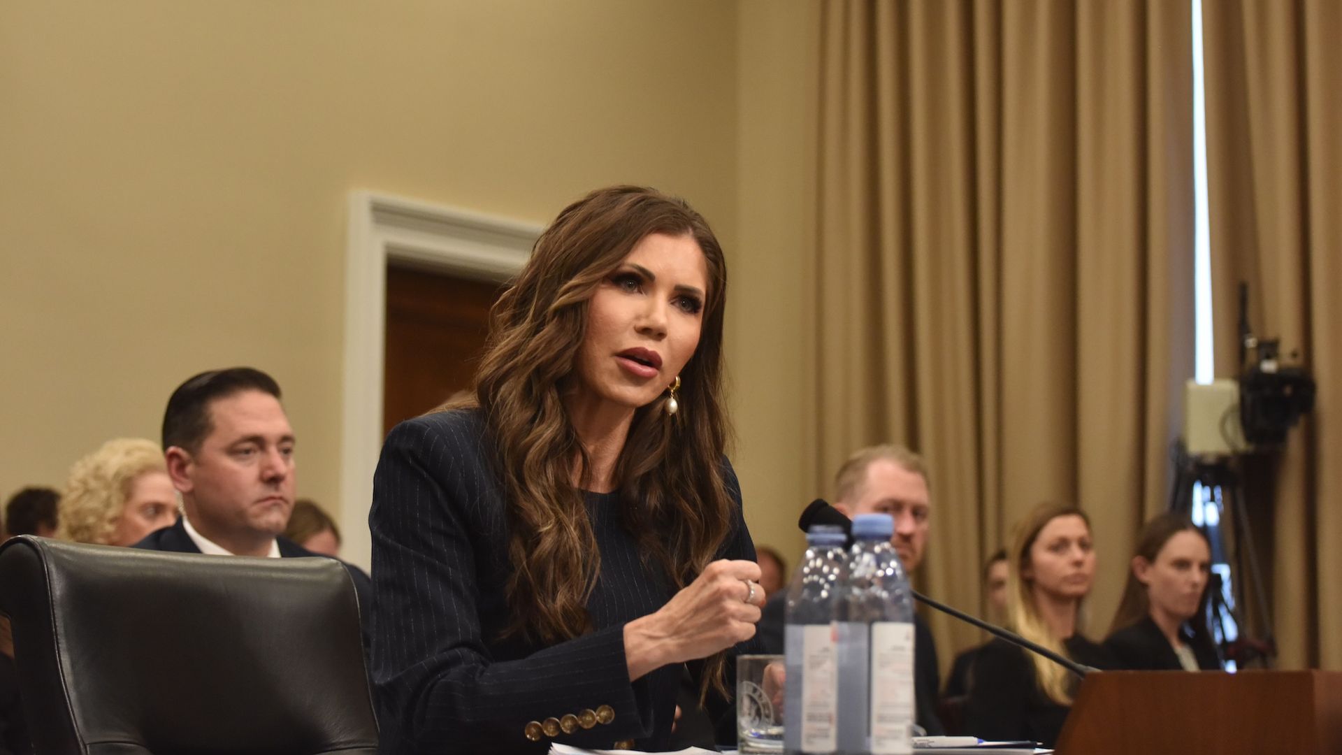 DHS Secretary Kristi Noem speaking at a congressional hearing with water bottles in front of her.