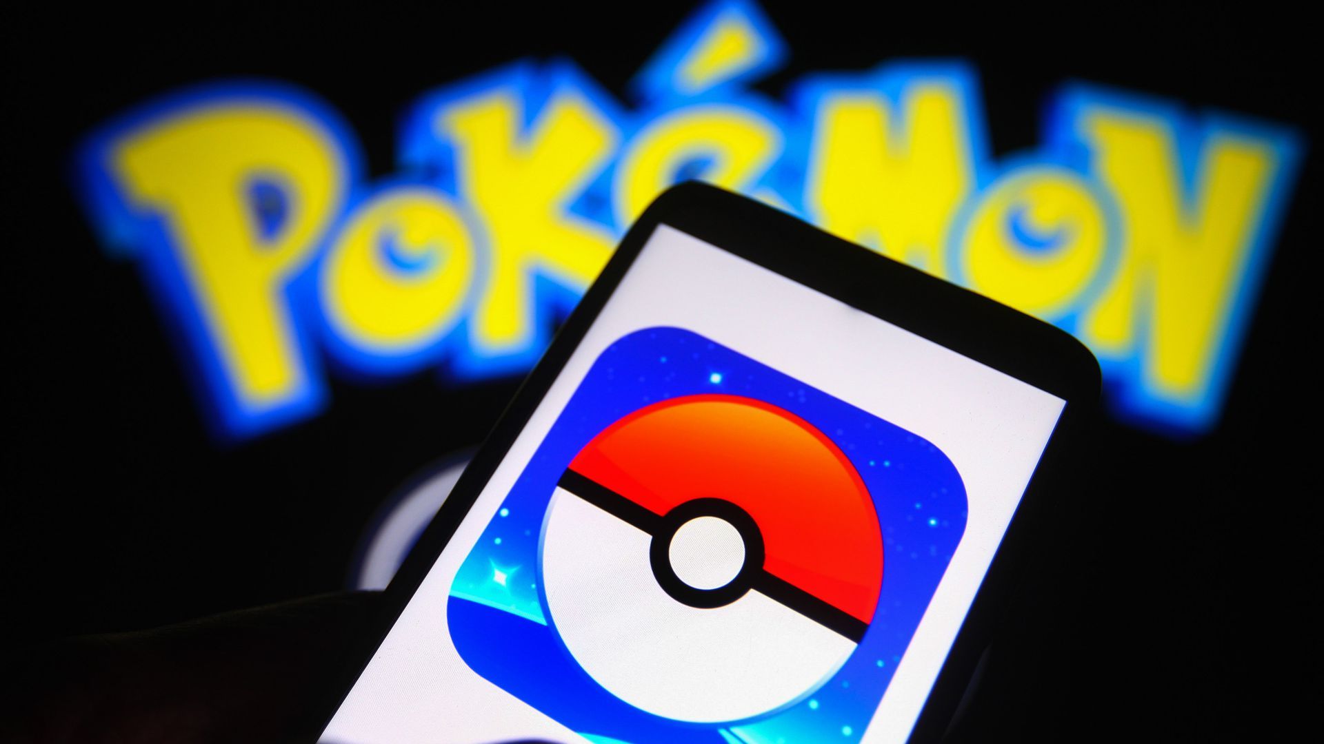 A phone showing a poké ball on its display in front of a Pokémon logo.