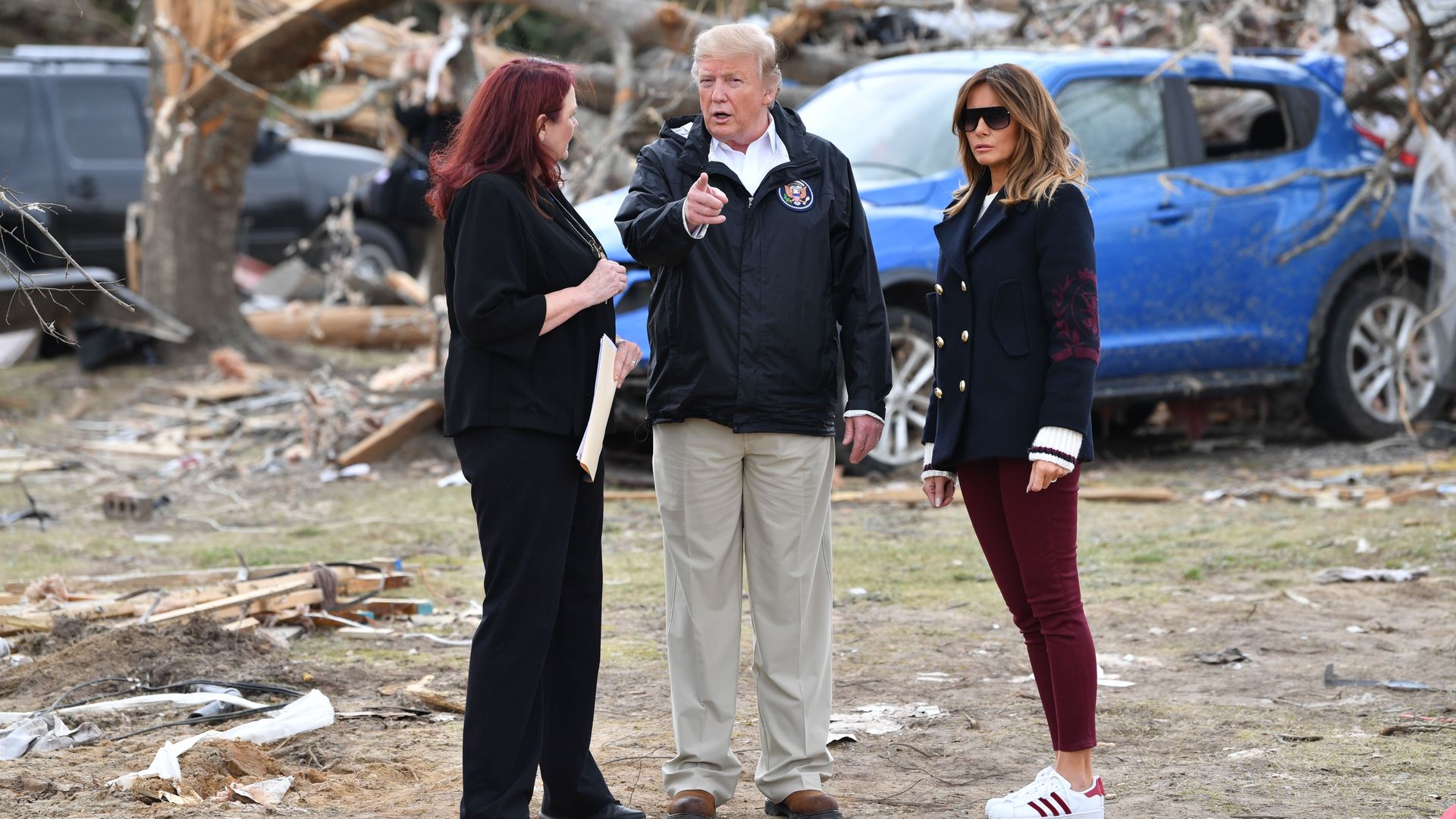 President Trump and wife Melania Trump stand next to a woman in front of rubble from a tornado in Alabama.