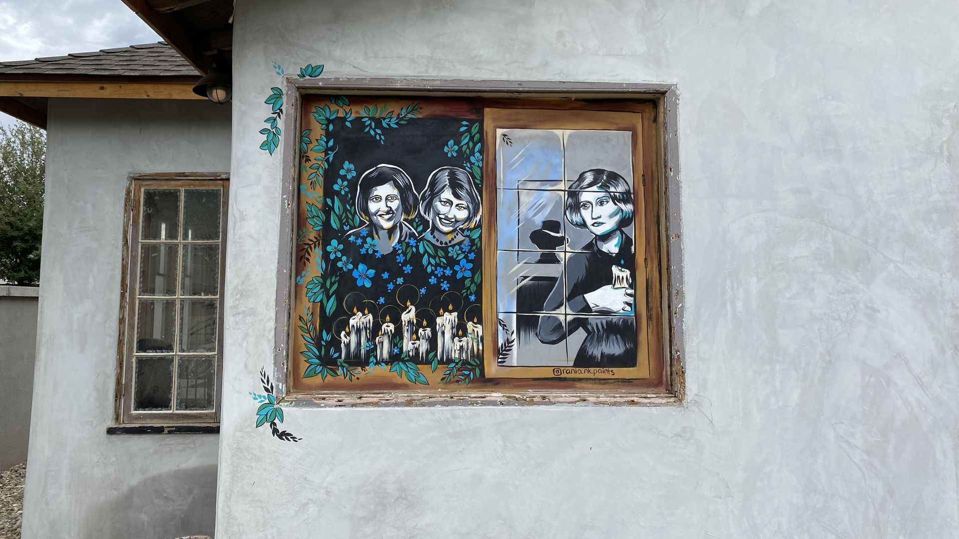 A window of a house with images of two women with candles in front of them on one side, and a woman with a mysterious man's silhouette behind her on the other side. 