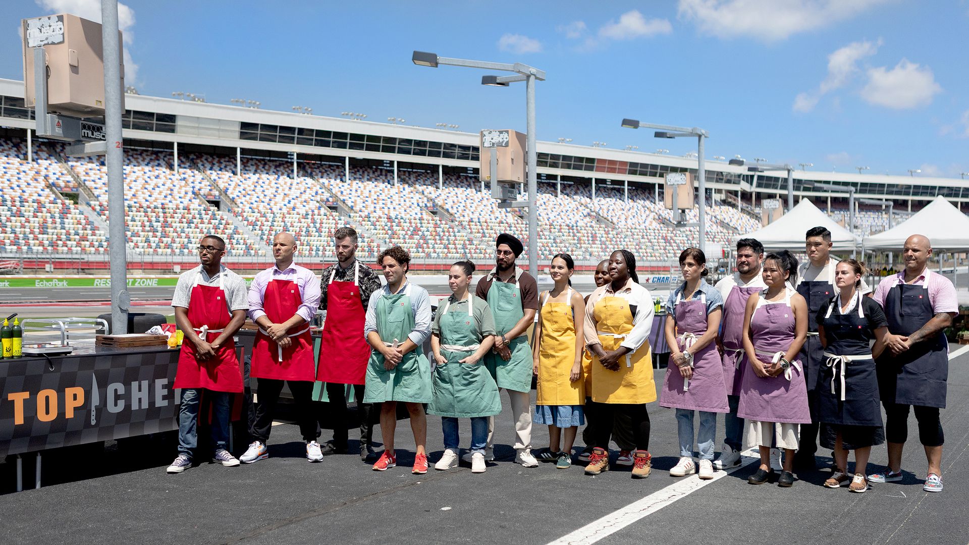 Chefs lined up in different color aprons on a race car track