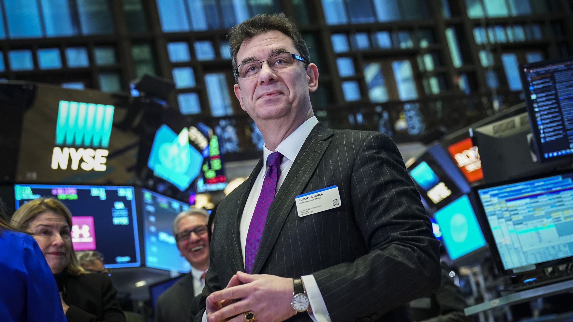 Albert Bourla standing on the floor of the New York Stock Exchange with trading monitors in the background.