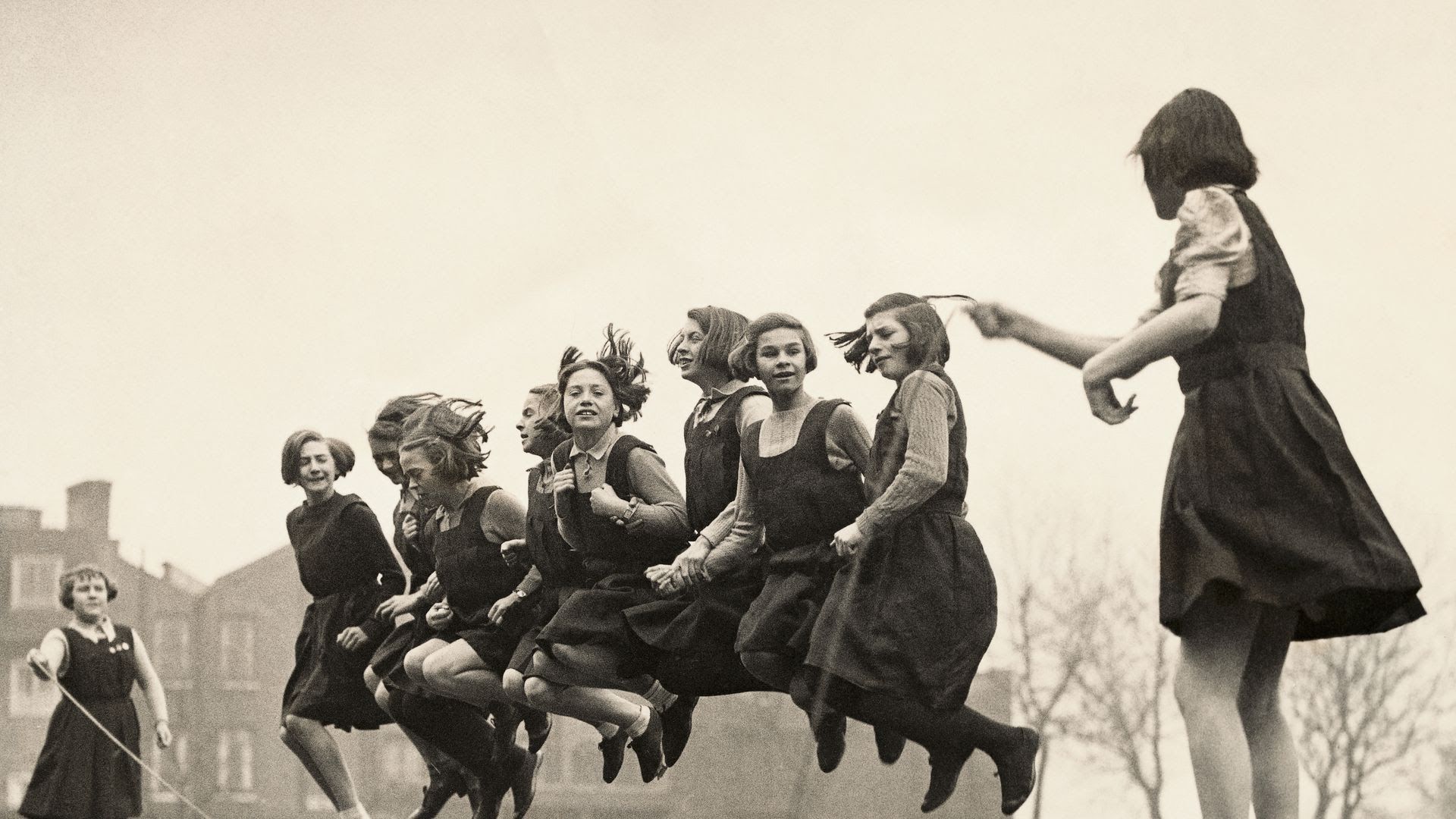 A black and white photo of schoolgirls in uniform jumping rope