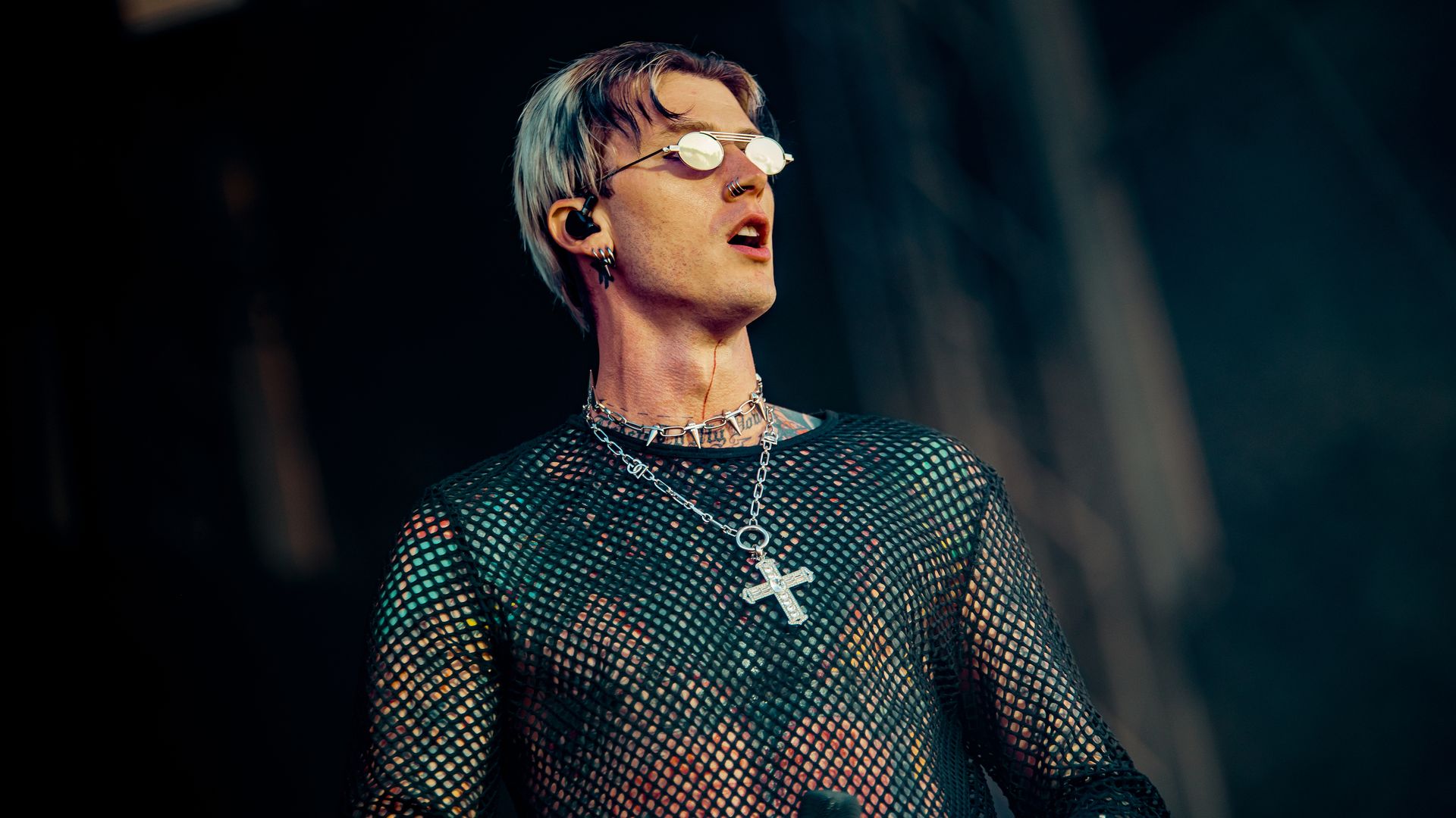 Machine GUn Kelly stands on a stage with sunglasses. 