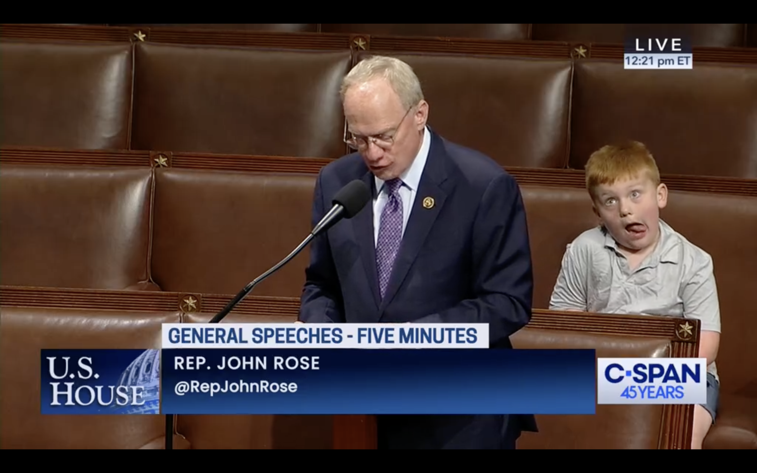 A child makes a silly face while a man speaks.