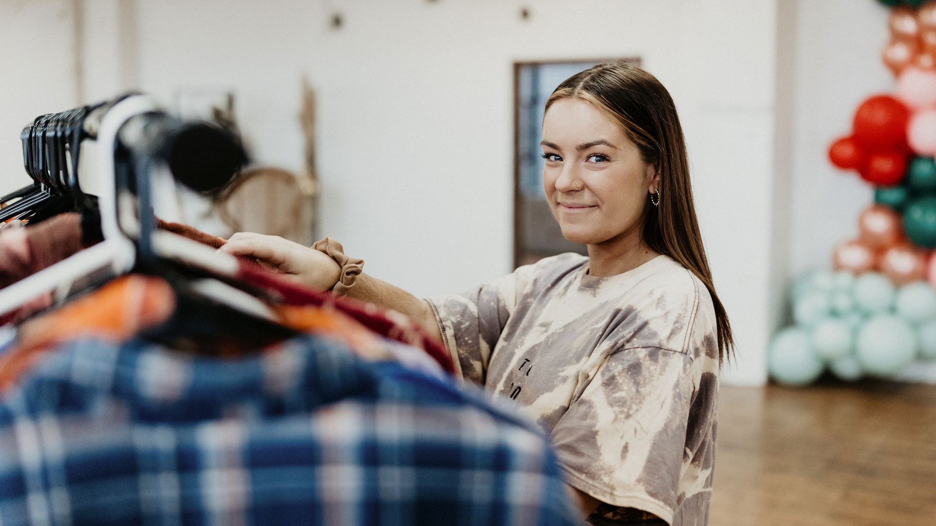 Fashion designer Rebecca Maxwell smiles at the camera as she goes through a rack of clothing at a studio space.