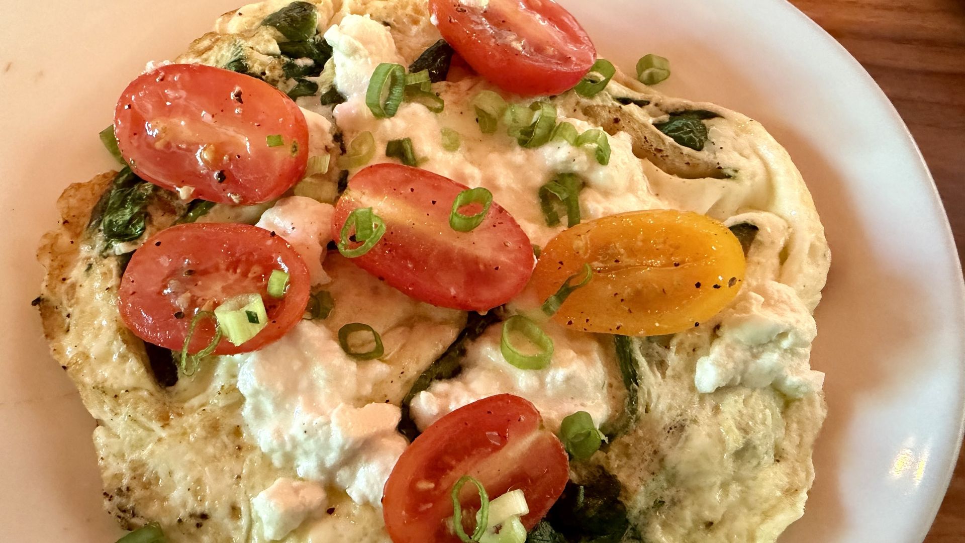 Close-up of a flatbread topped with creamy white sauce, halved cherry tomatoes, and chopped green onions on a white plate.