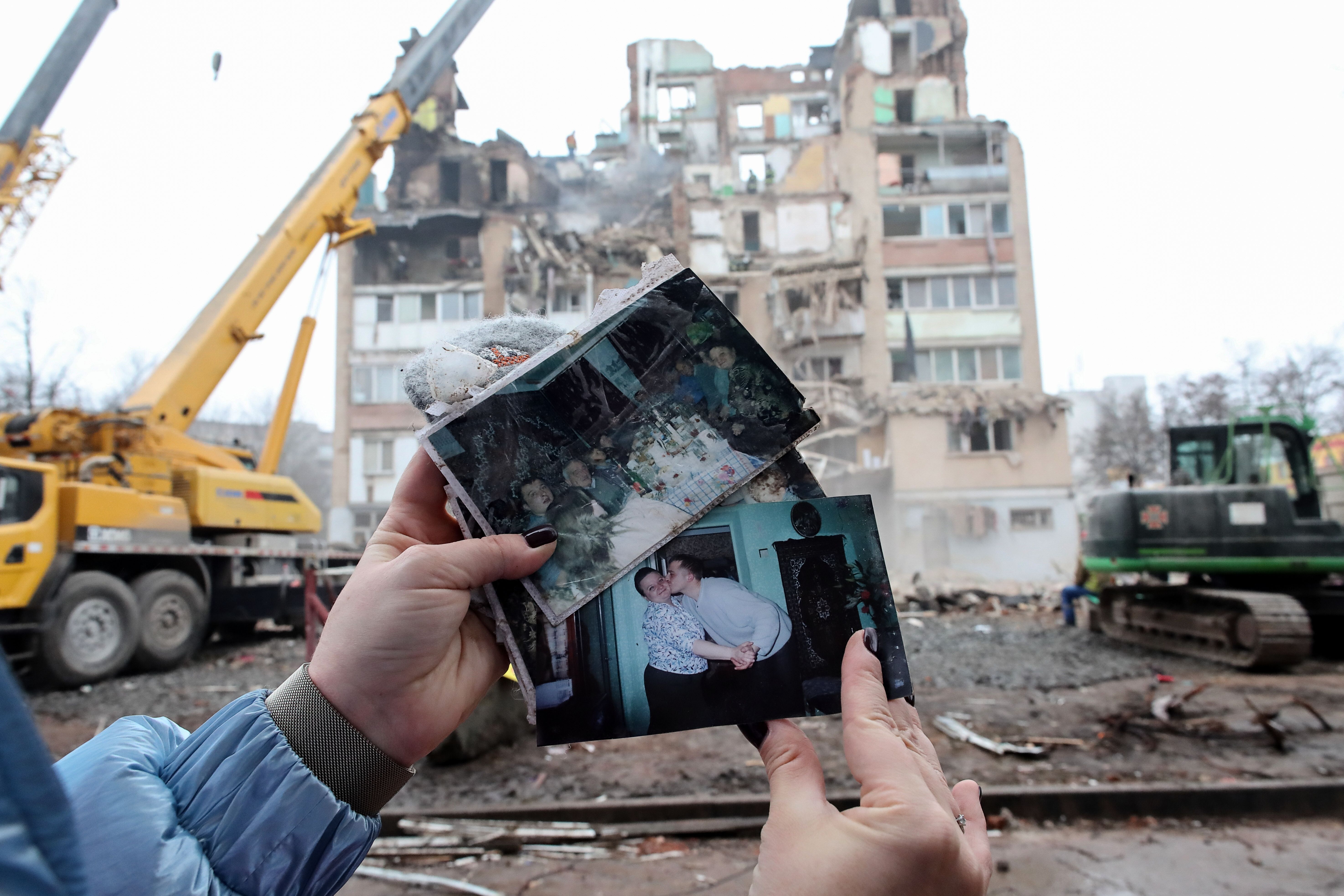 A woman holds up photos in front of a damaged building